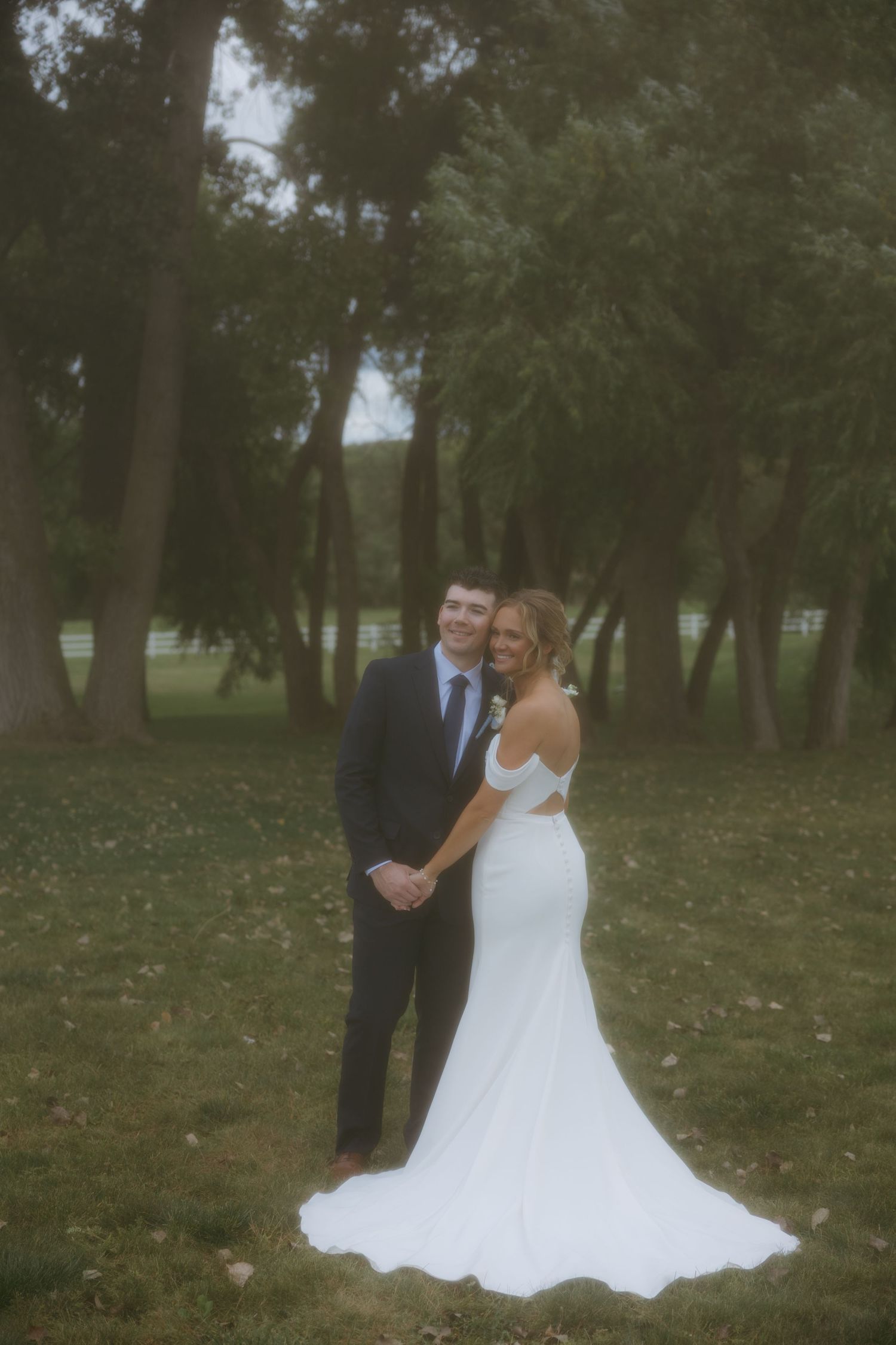 A couple shares a romantic moment in a wooded park setting, with the bride wearing a flowing white wedding gown.