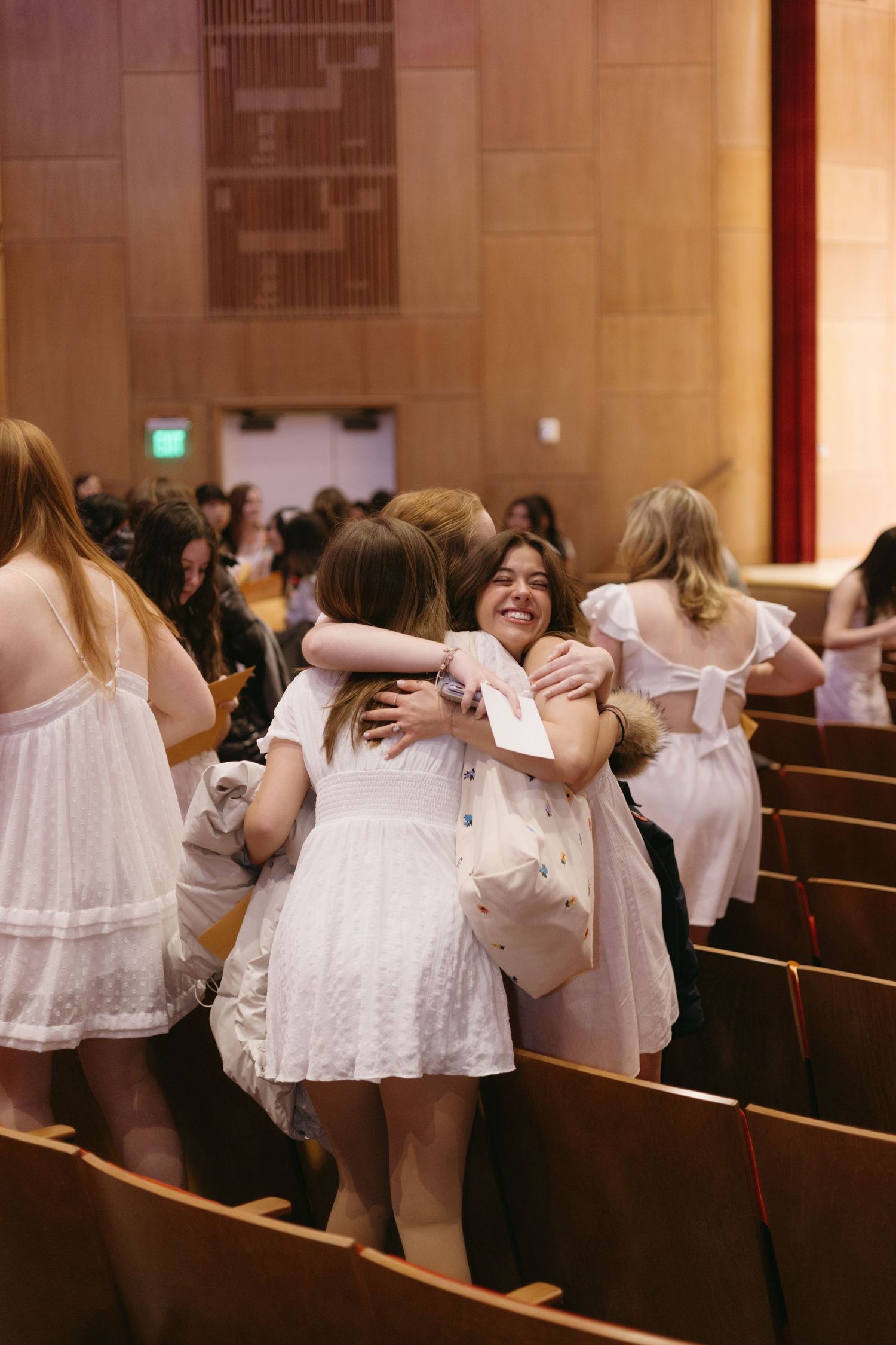 Group of people in white dresses embracing and celebrating in church pews during a joyful gathering.