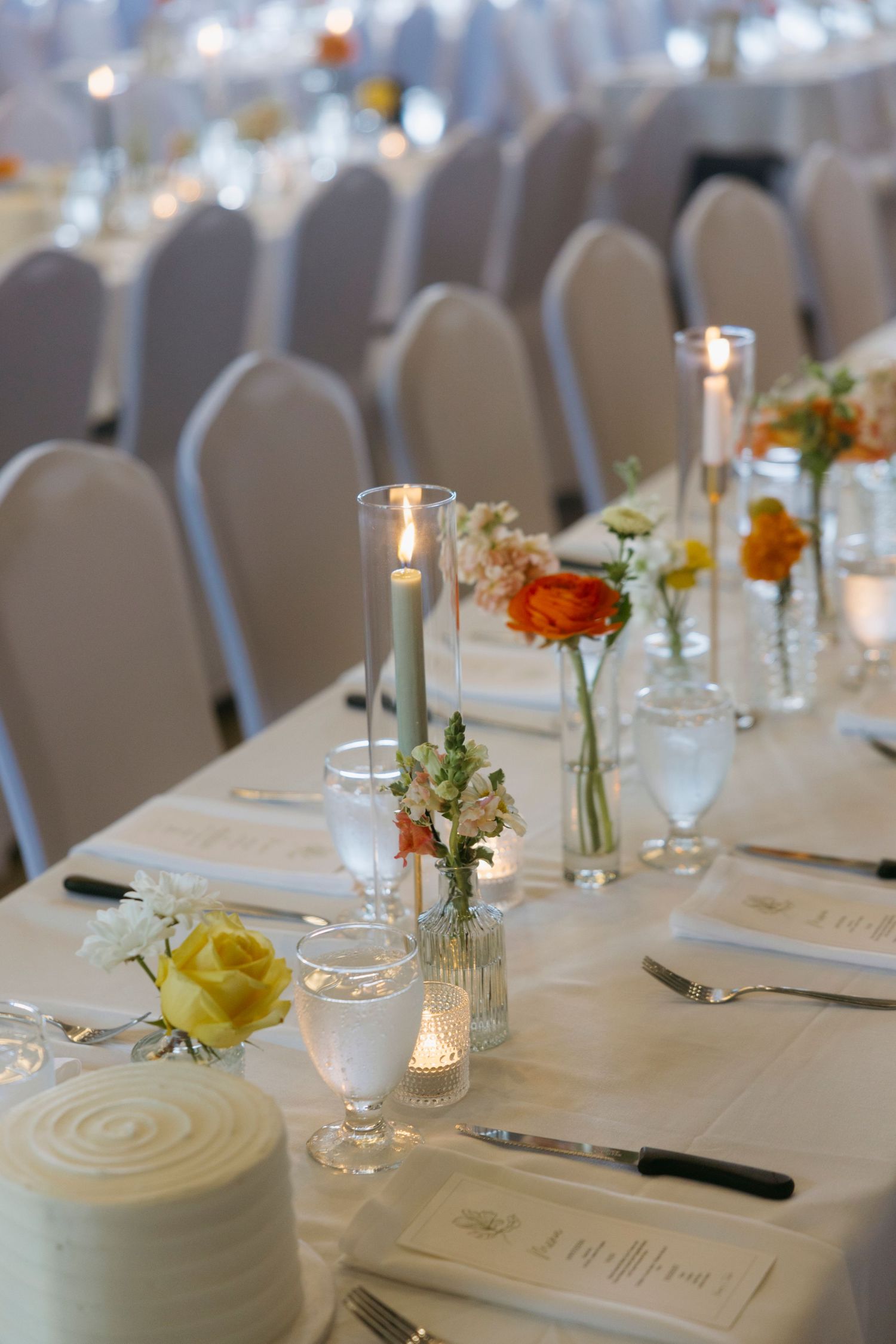 Elegant wedding reception table set with white linens, candles and delicate floral centerpieces in glass bud vases.