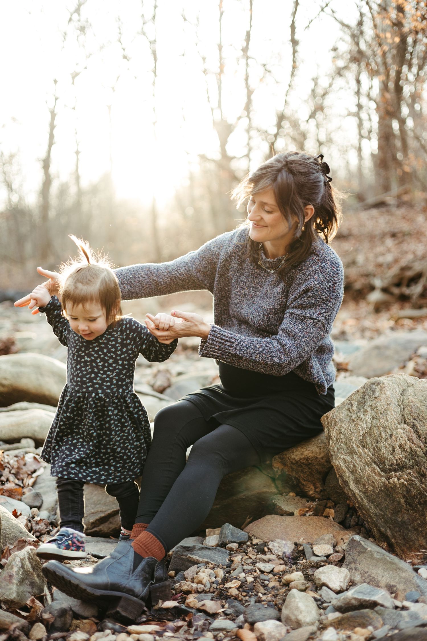 Parent and small child play together on rocks by stream at sunset.