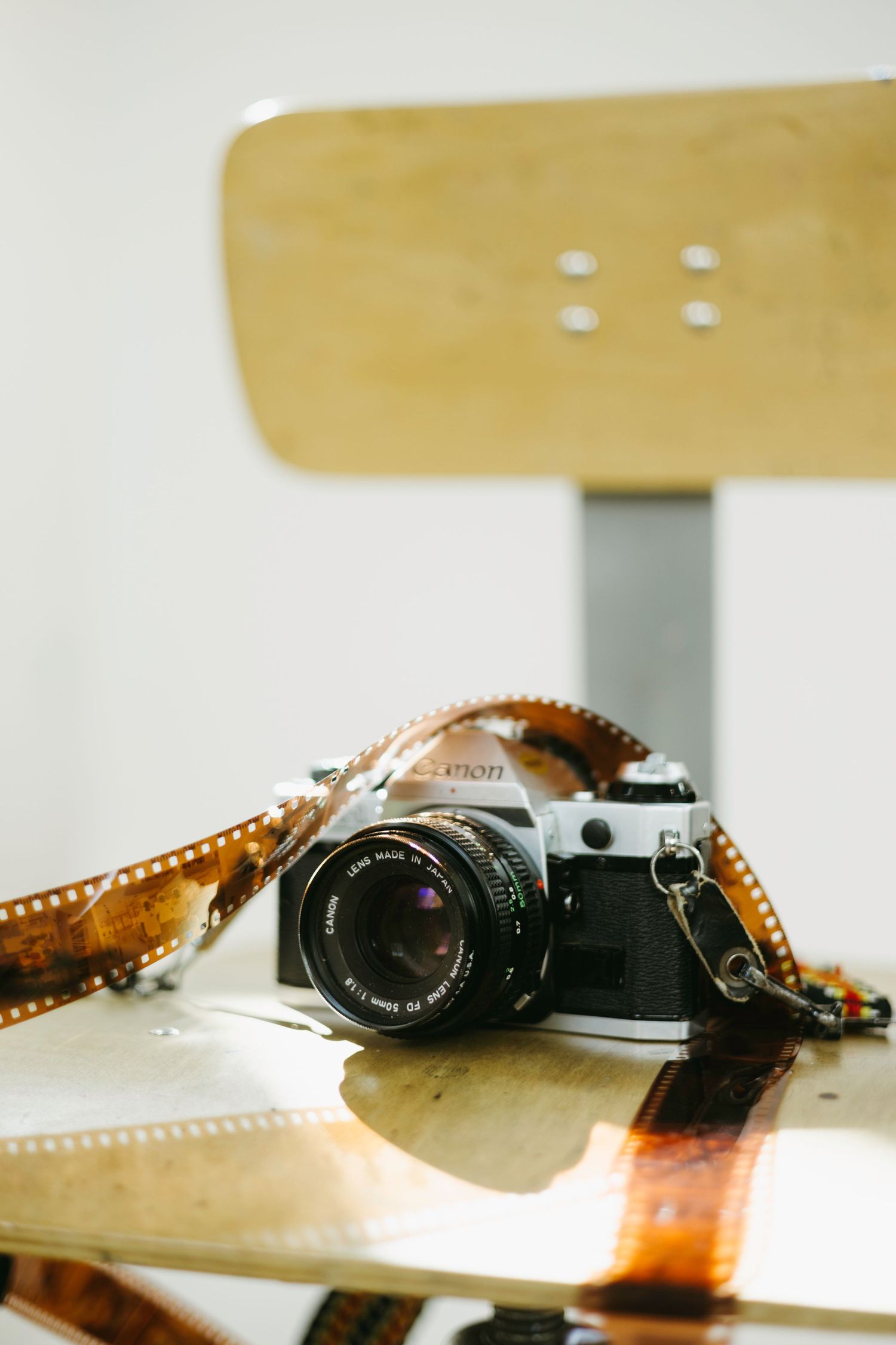 Vintage film camera with 50mm lens sits beside exposed analog film negatives on wooden surface in natural light.