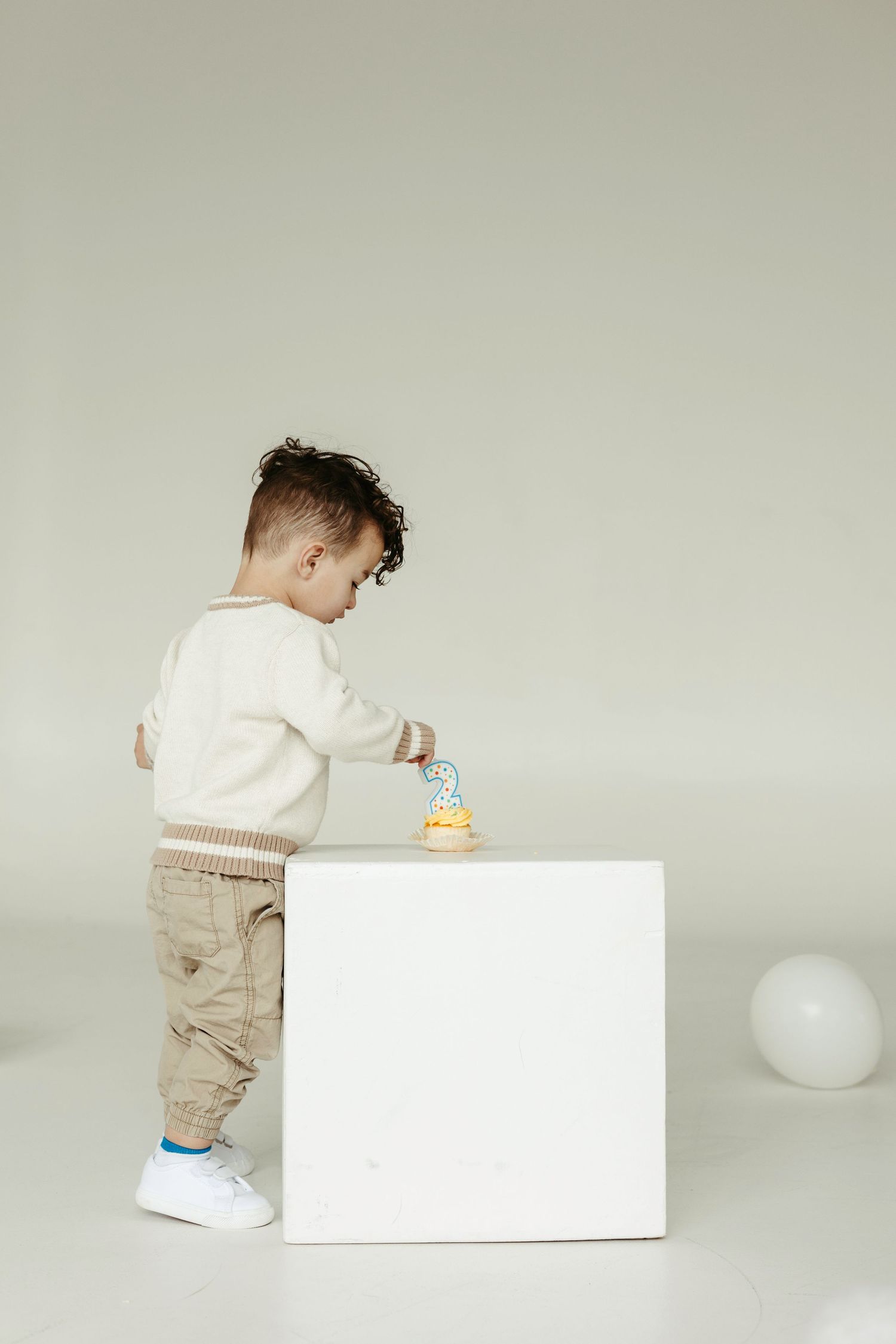 A small child in casual attire stands placing something on a white cube pedestal against a neutral background.