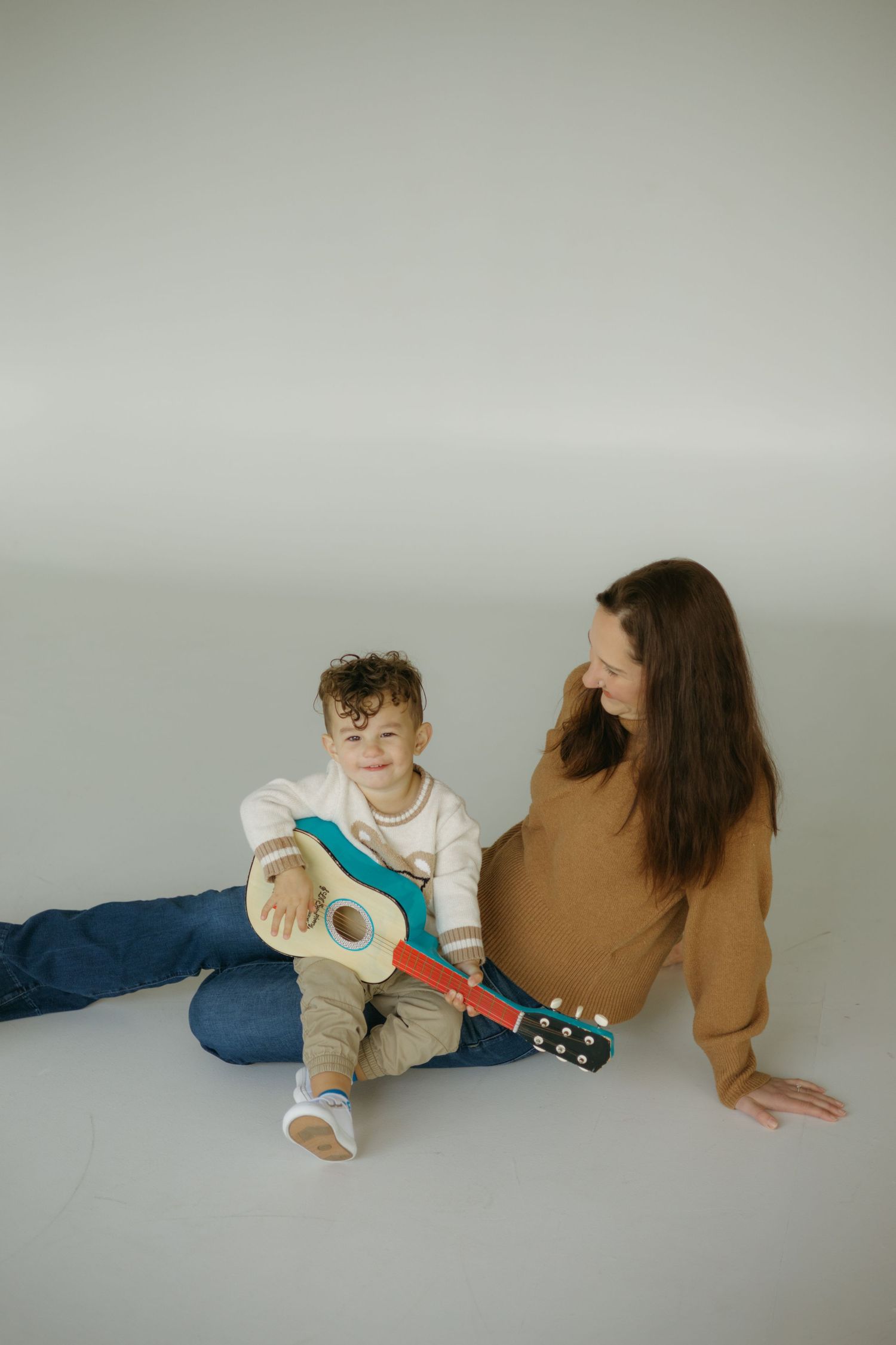 Two people sitting on floor with guitar creating a minimalist artistic composition against neutral background.