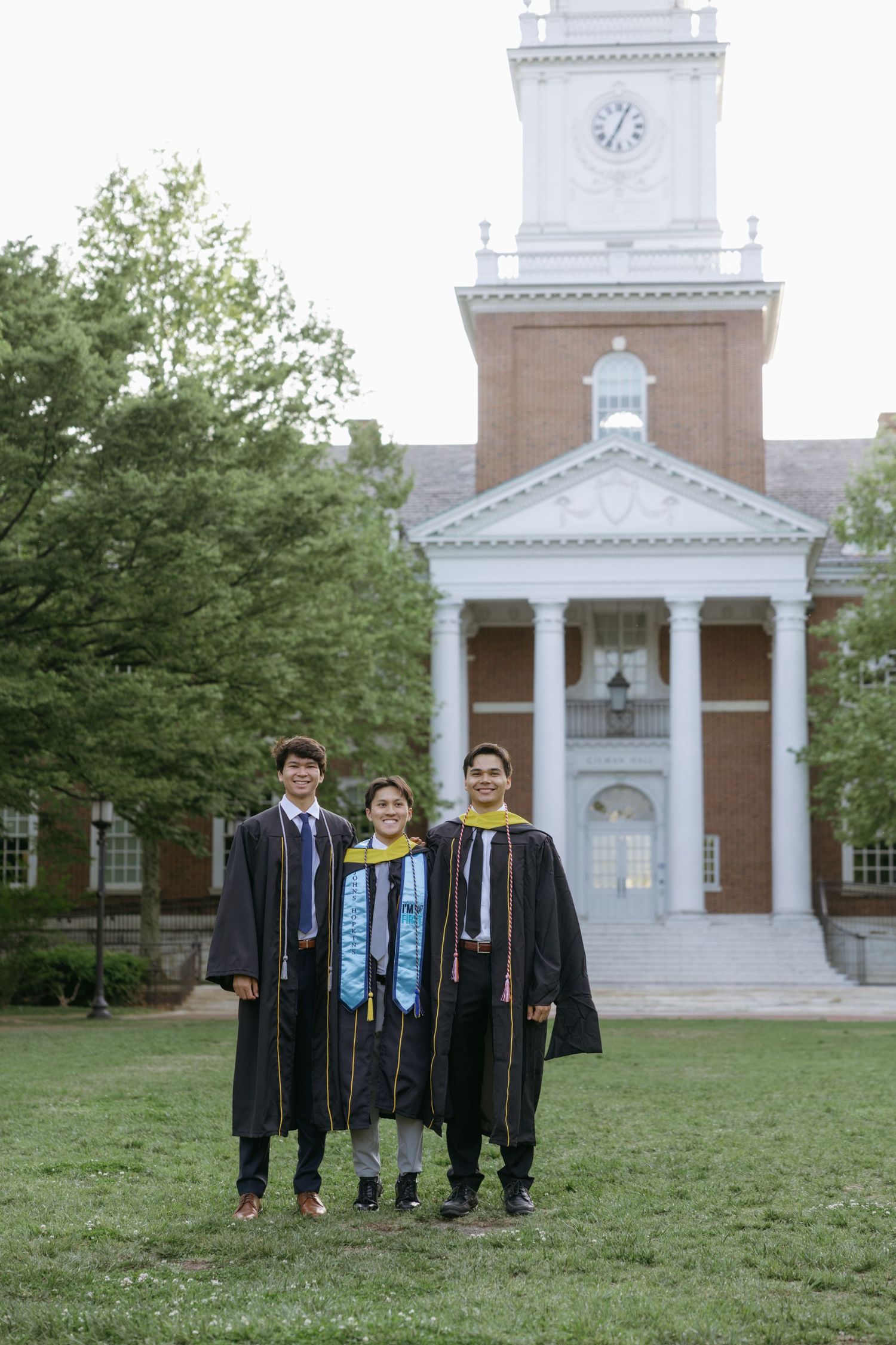 Graduation ceremony in front of a stately brick building with white columns and clocktower on a spring day.