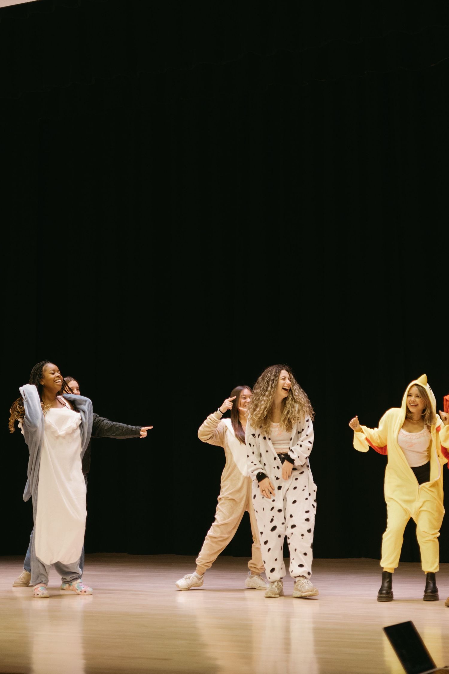 Dancers dressed in white and yellow costumes perform a dynamic contemporary routine on a dark stage.