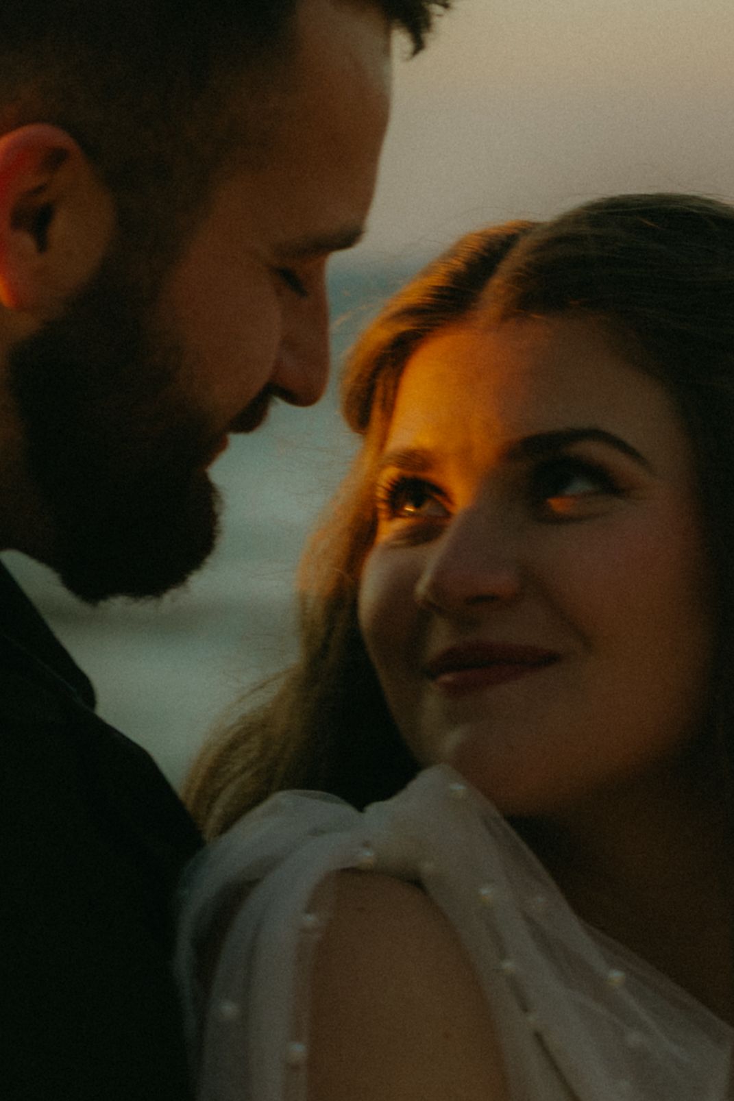 A romantic close-up portrait of a couple sharing an intimate moment at sunset with warm lighting and soft focus.