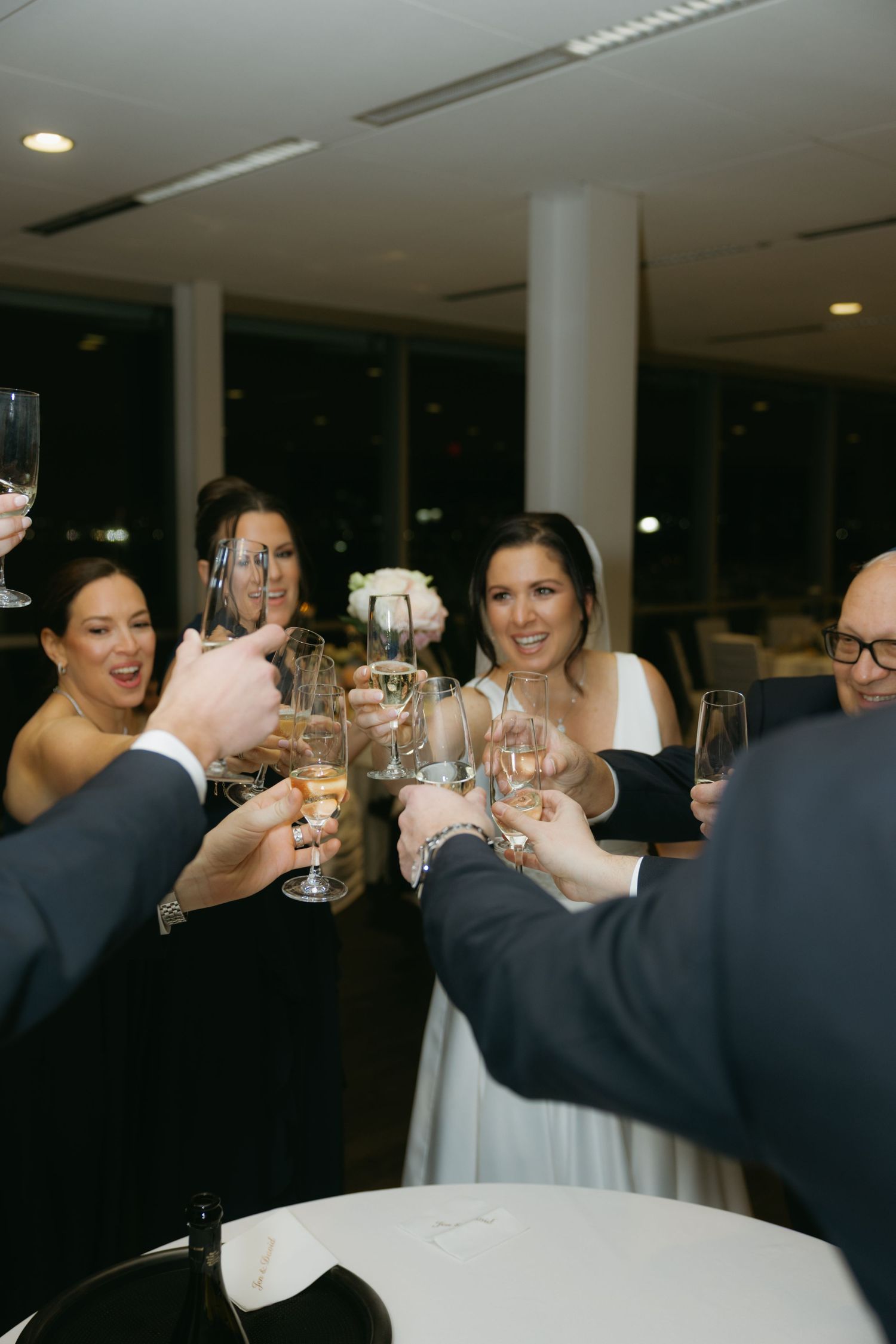 Wedding guests raise their glasses in a celebratory toast during an indoor reception.