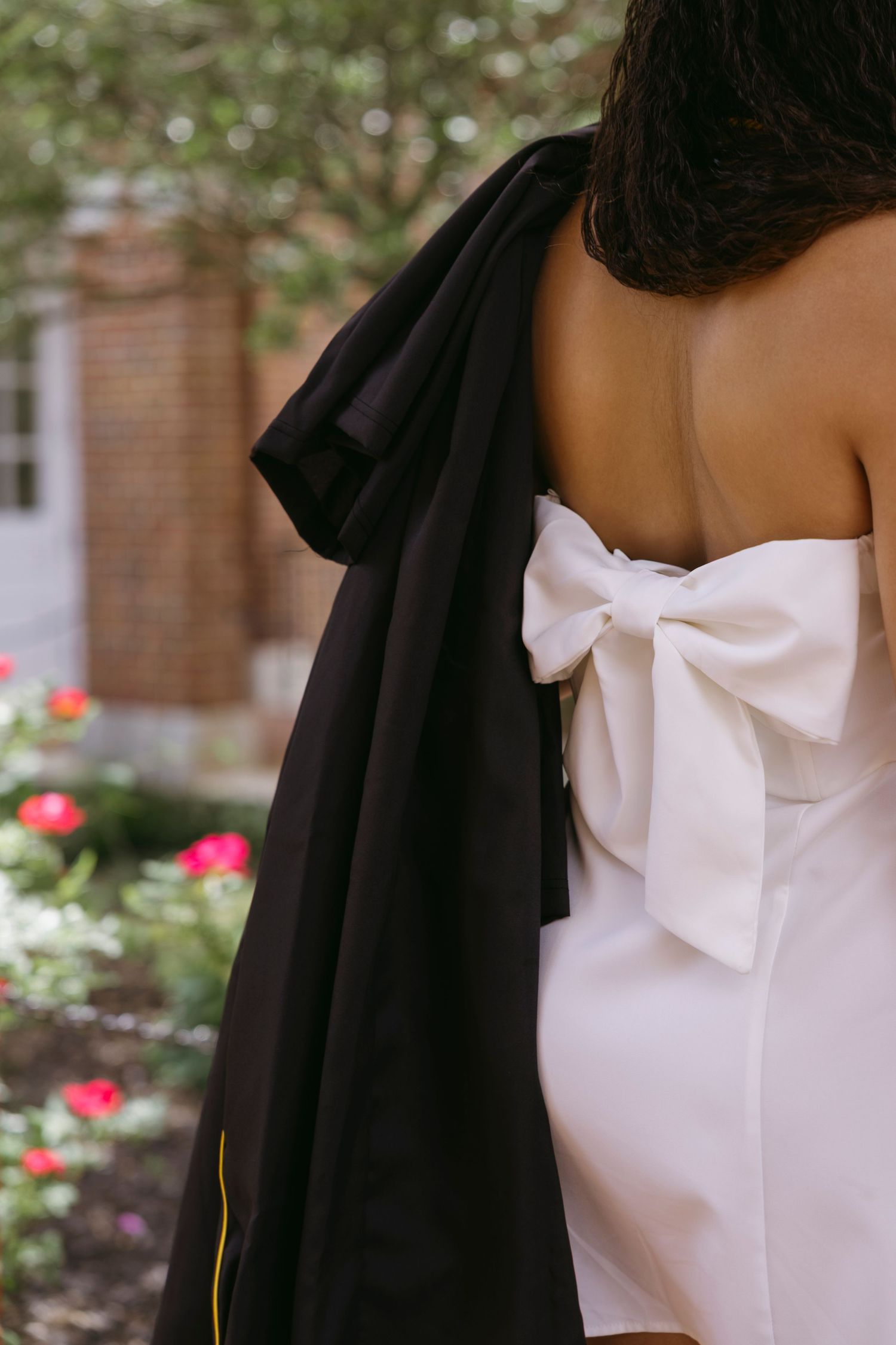Close-up detail of a white strapless dress with a large decorative bow against a black draped fabric outdoors.