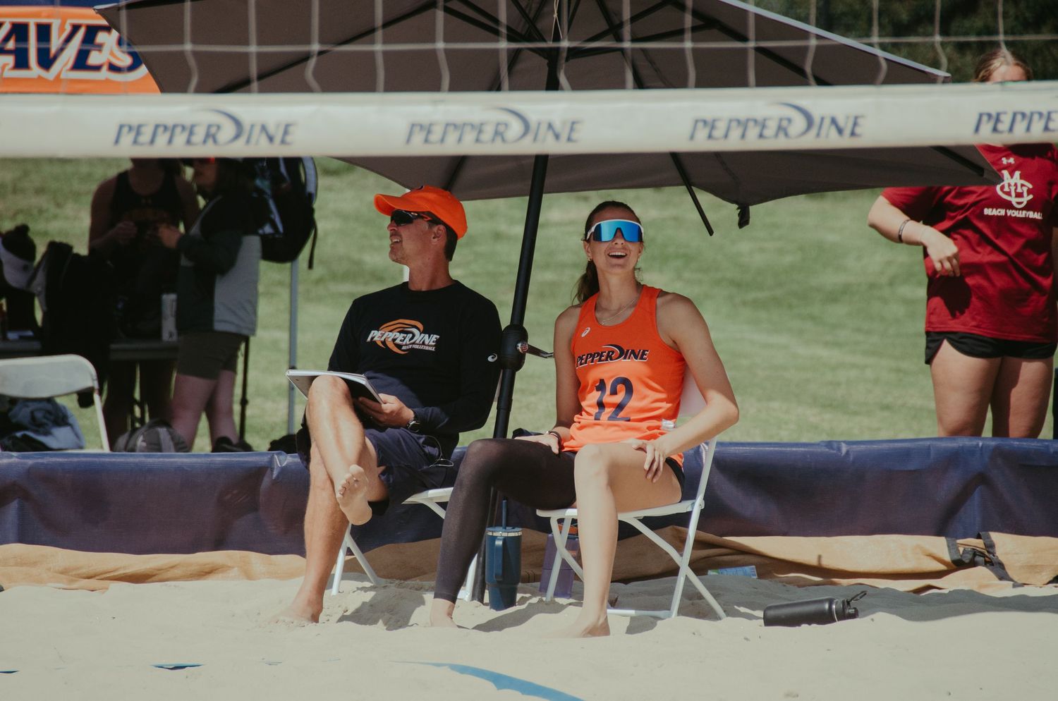 Athletes resting in folding chairs under a sports tent during an outdoor event.