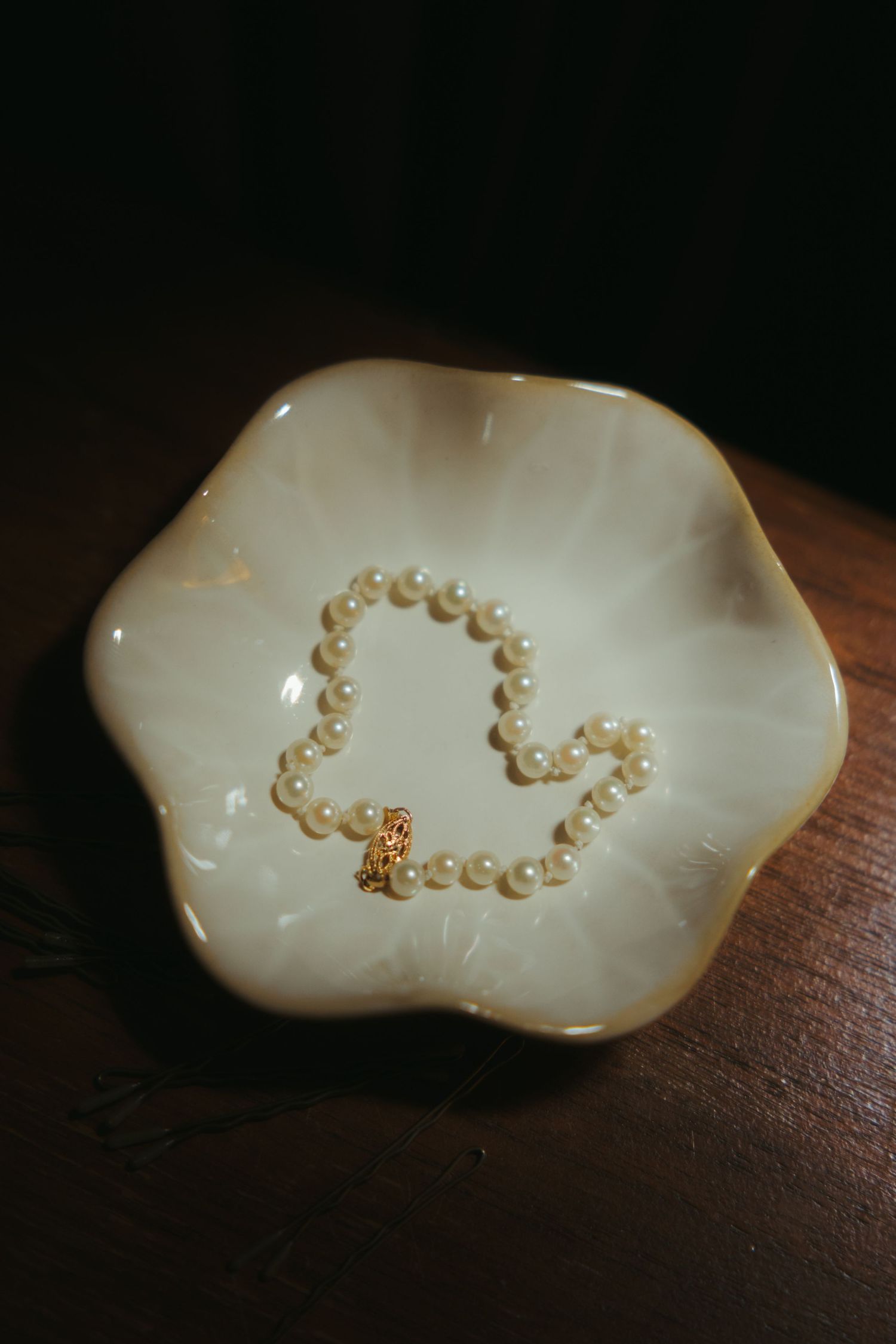 Small white pearls arranged in a heart shape on a pearly white surface against a dark wooden background.