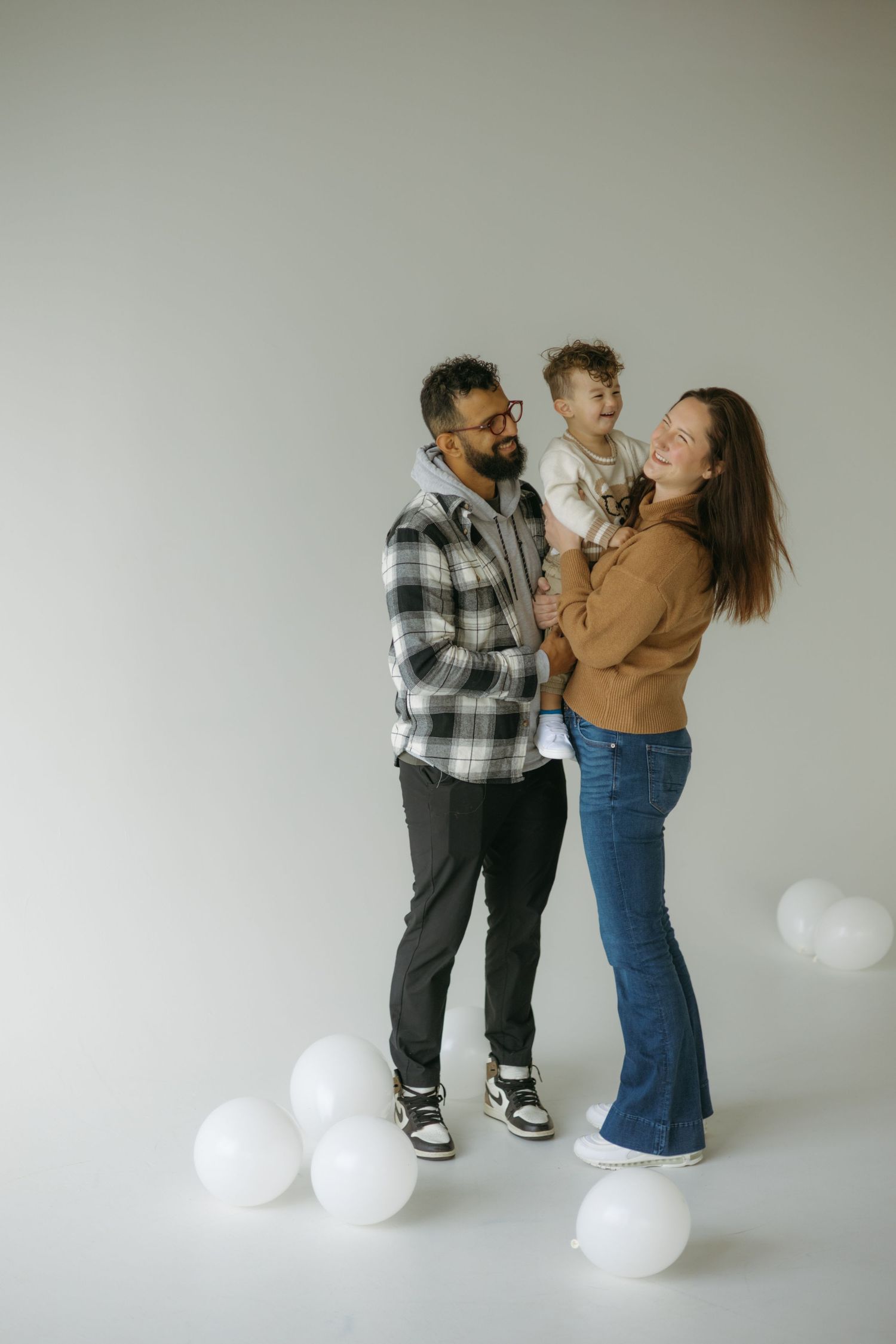 Three candid photos show a couple playfully interacting against a white backdrop with white balloons on the floor.
