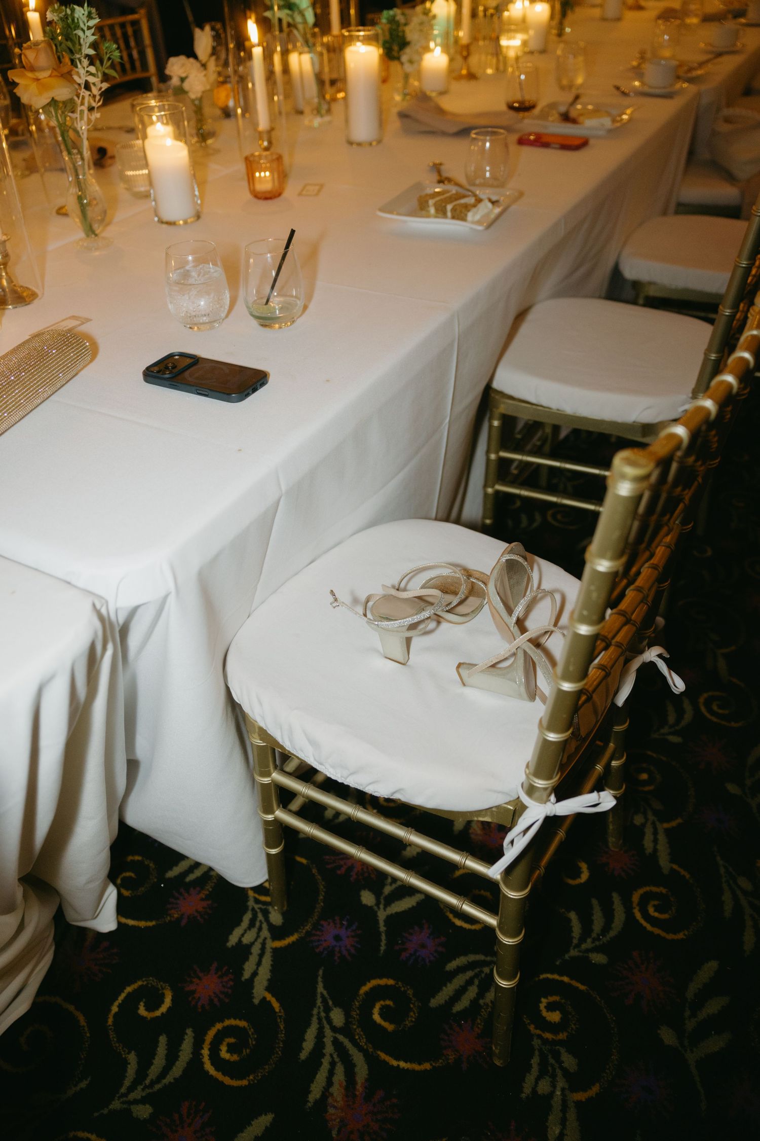 Gold chiavari chairs with white cushions surround an elegant candlelit wedding reception table with floral arrangements.