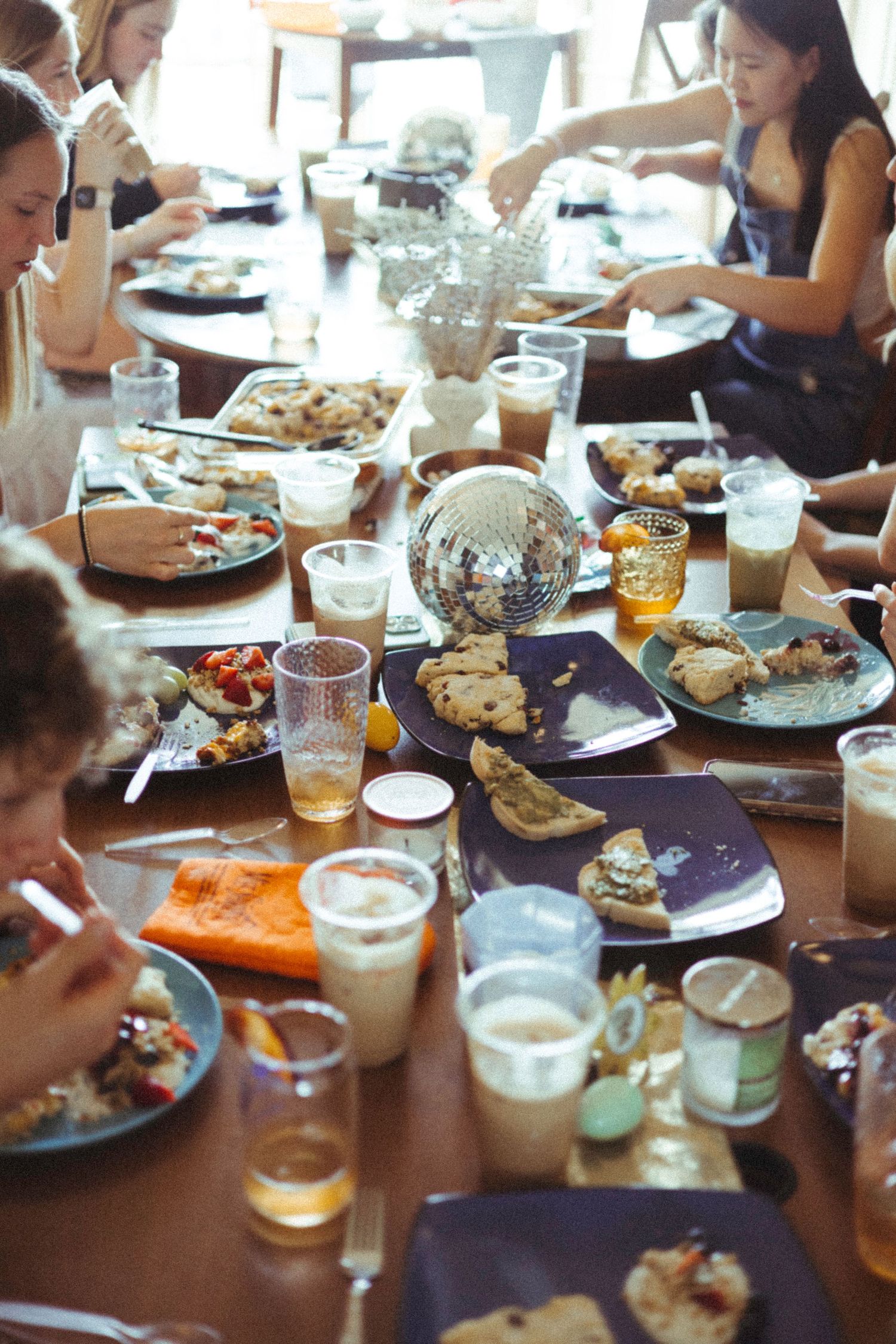 A casual dinner party with beverages and food served on purple plates around a wooden table.