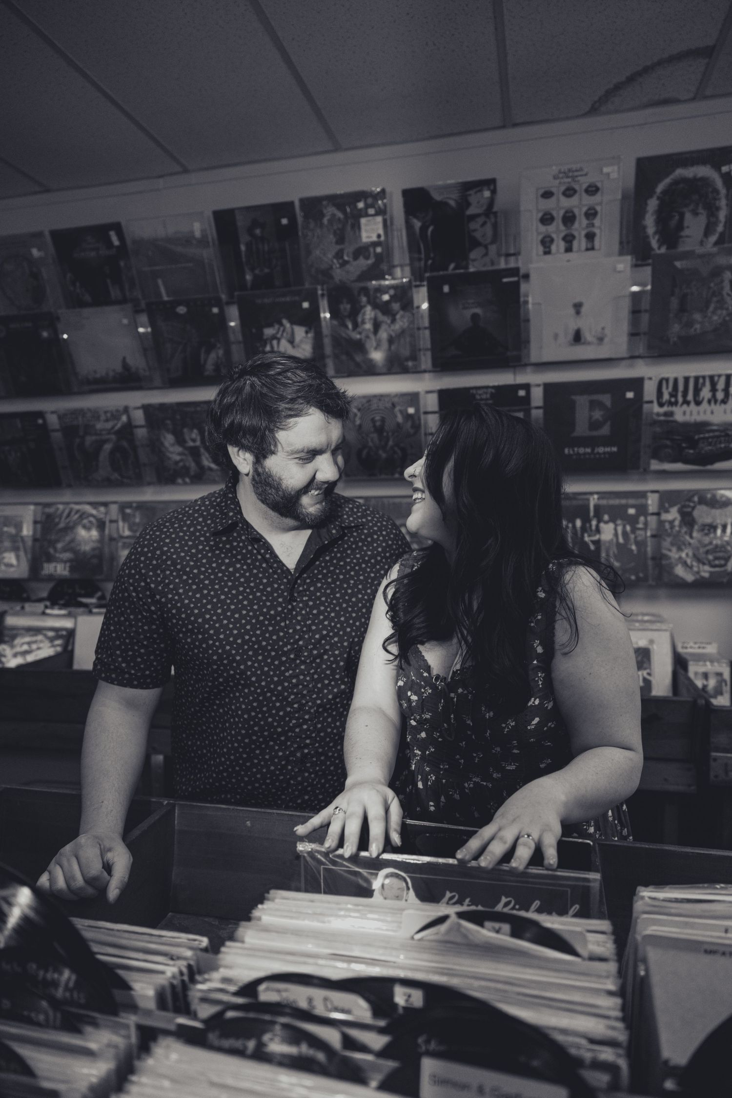 A couple browses through vinyl records together at a record store with album covers displayed on the wall.