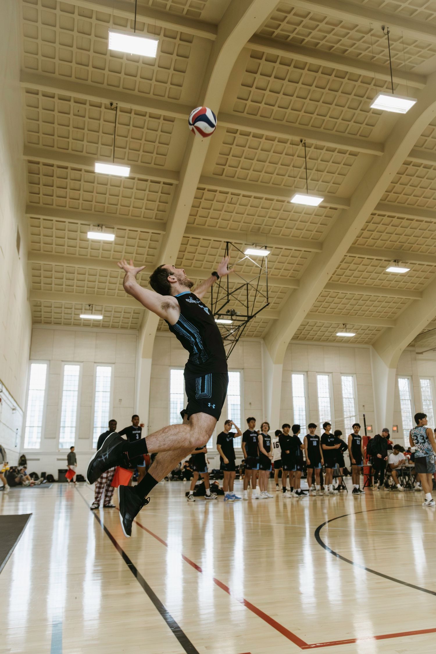 A volleyball player leaps high to serve the ball in an indoor gymnasium during a match or practice session.