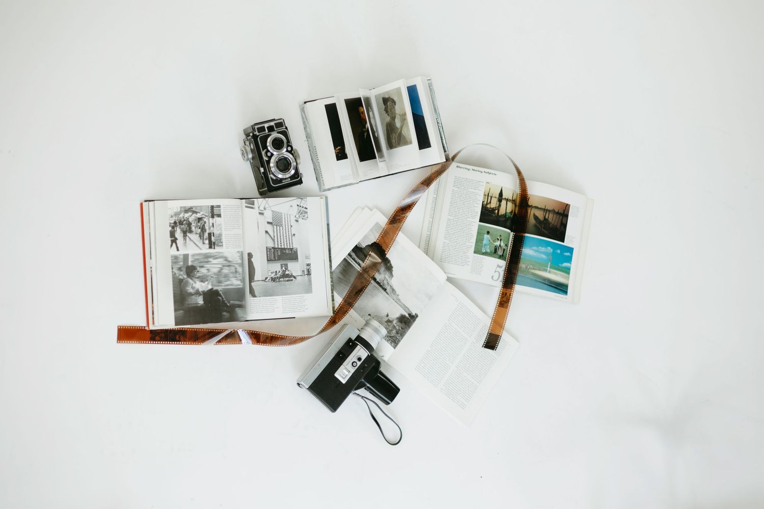 Vintage camera equipment, photographs, and pens scattered on a white surface against a minimalist background.