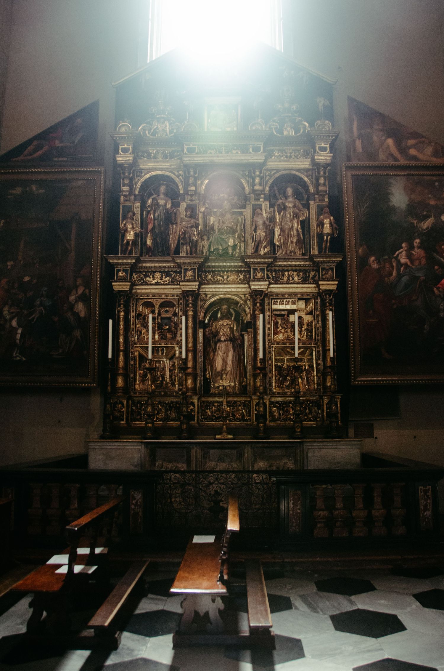 Elaborate golden altar piece with religious paintings and sculptures in a dimly lit church interior.