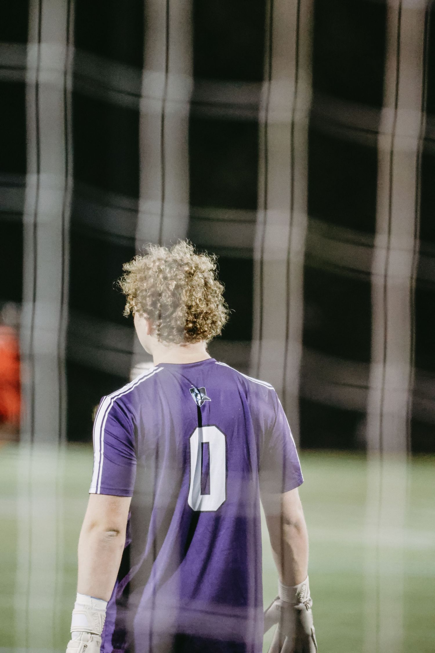 Athletic player in purple jersey number 0 viewed from behind against dark background.
