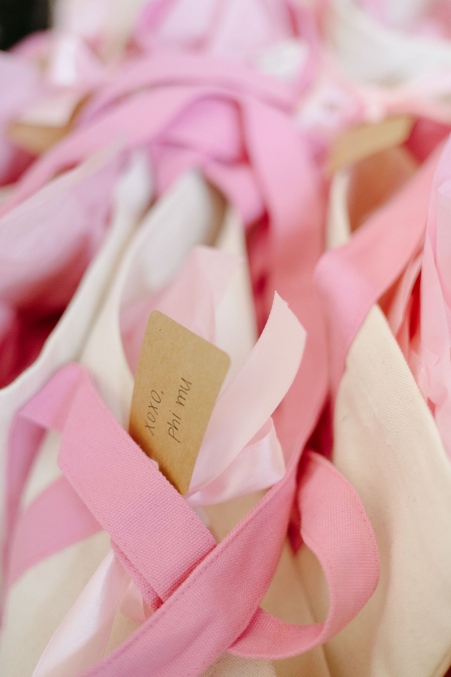 Pink and white ribbon strands intertwined with small paper tags for delicate wedding or party decor.