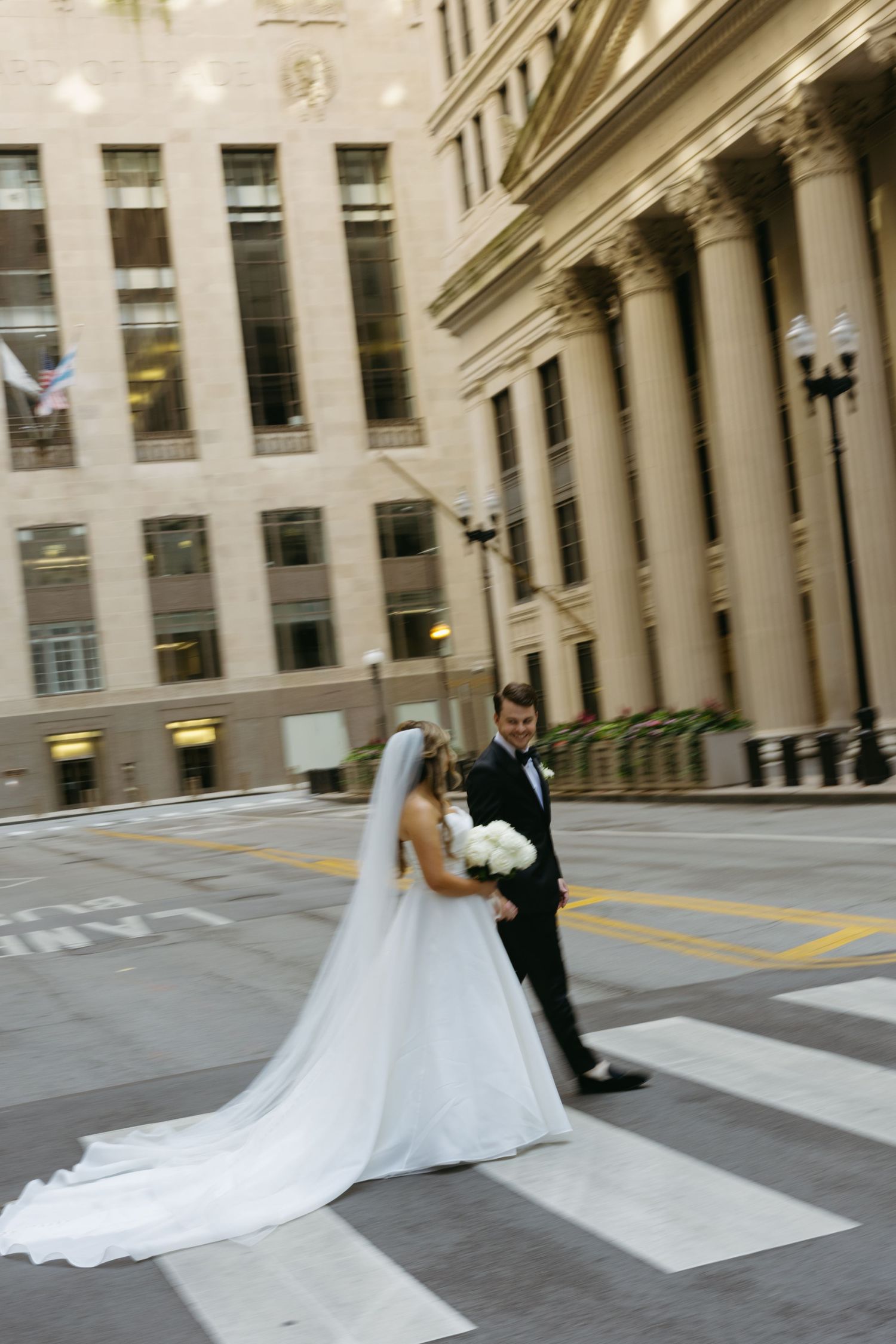 A wedding couple poses for romantic photos on a city street with elegant architecture in the background.