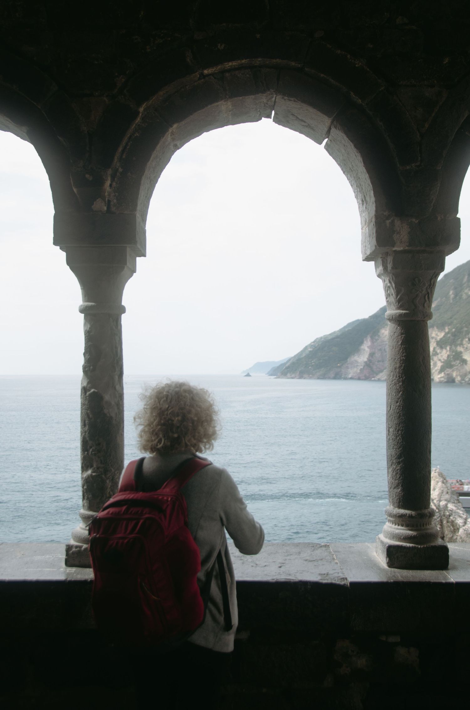 View of coastal cliffs through stone arches with someone looking out at the sea.