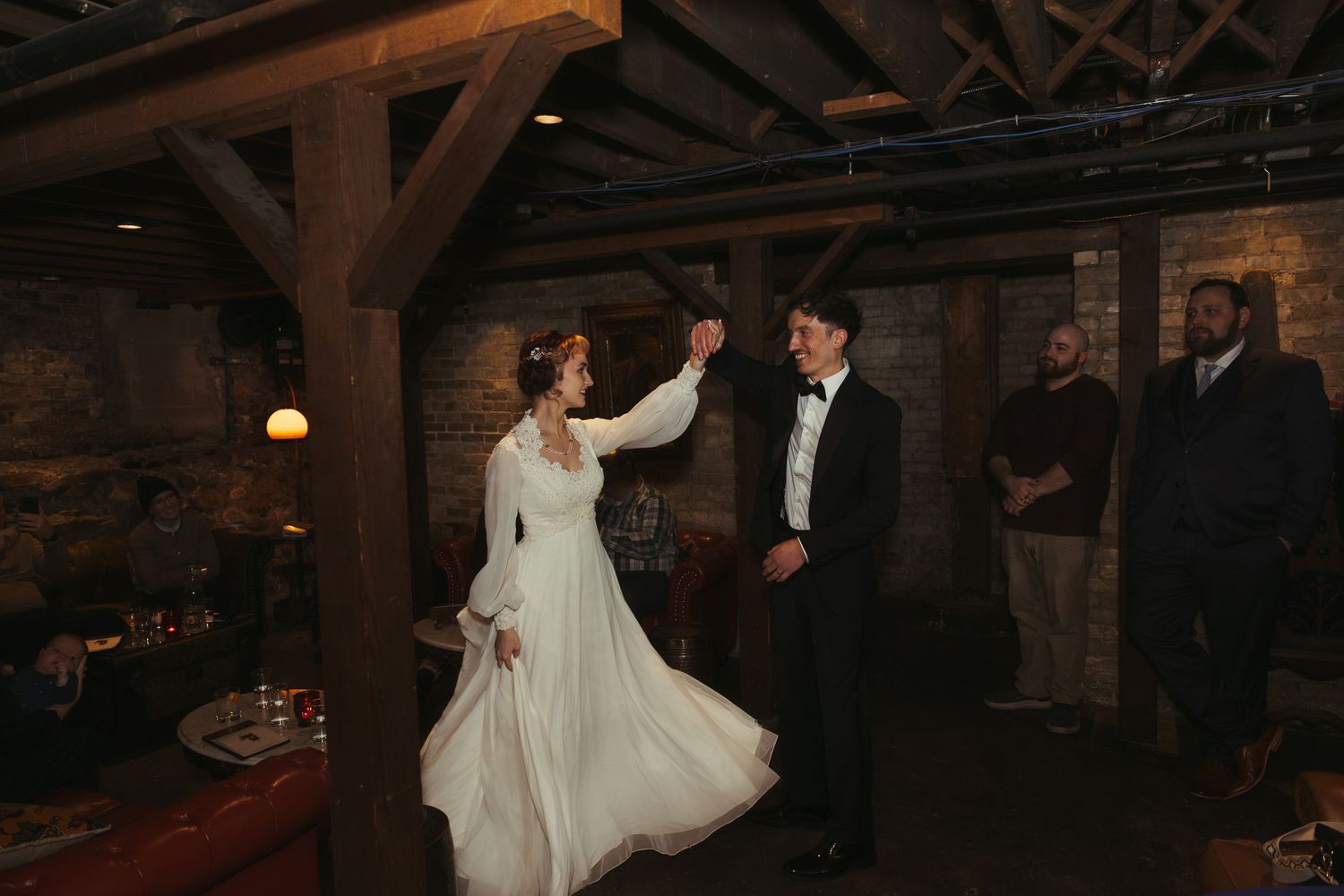 A couple shares their first dance in a rustic barn venue with exposed wooden beams and warm lighting.