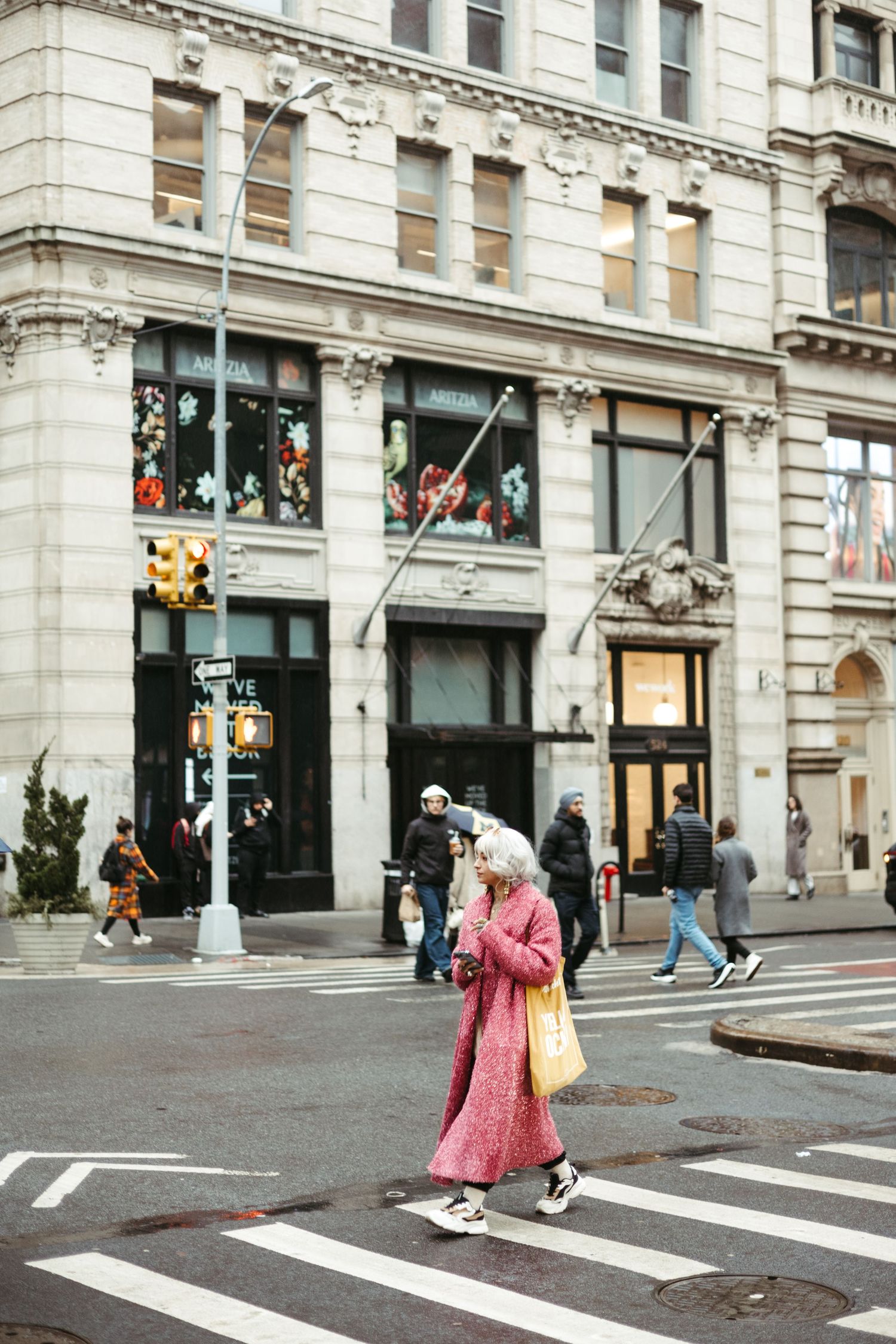 A pedestrian in a pink coat crosses a busy city street in front of a historic stone building in Manhattan.