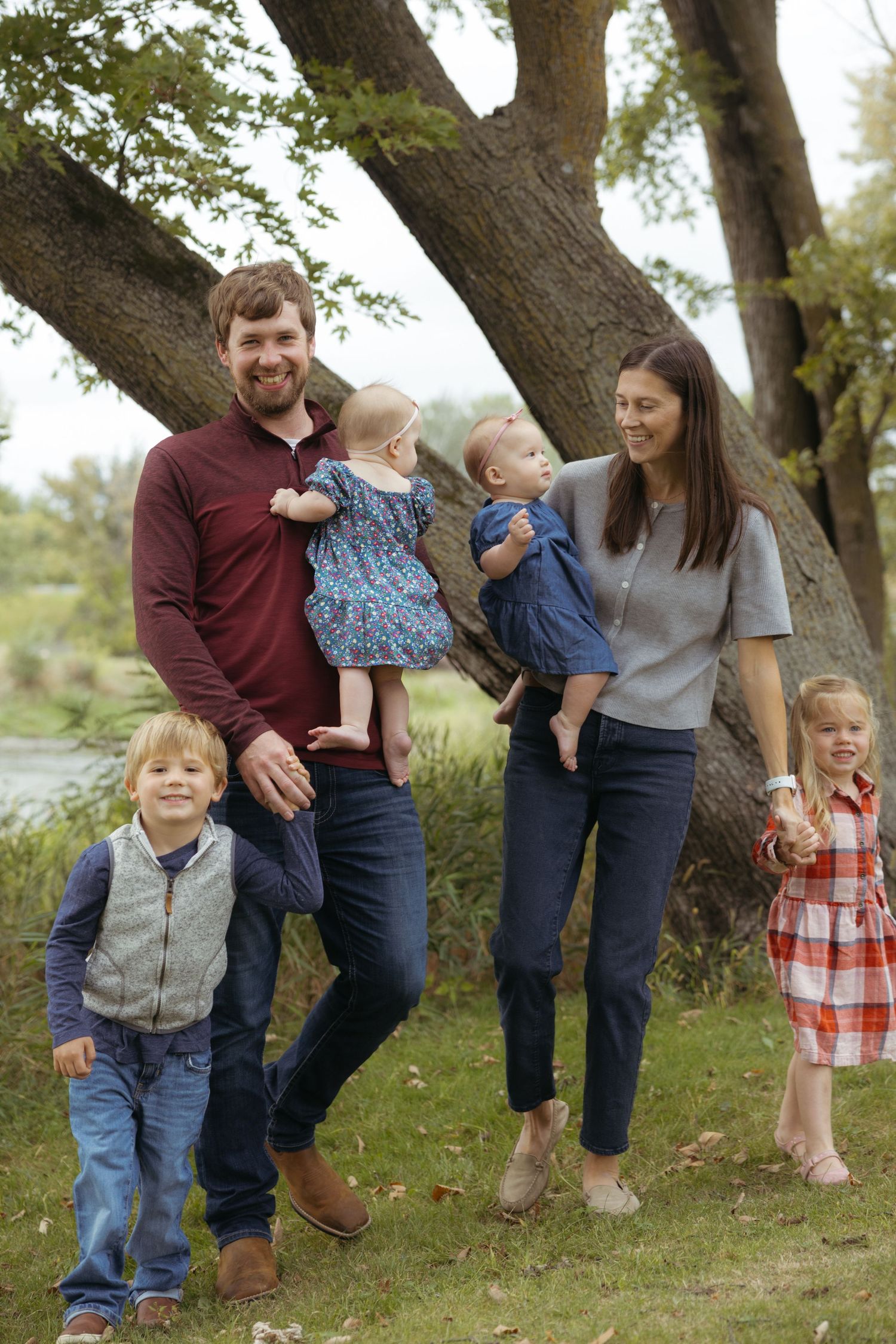 Family having fun outdoors together while wearing casual clothes beneath a large tree in a natural setting.