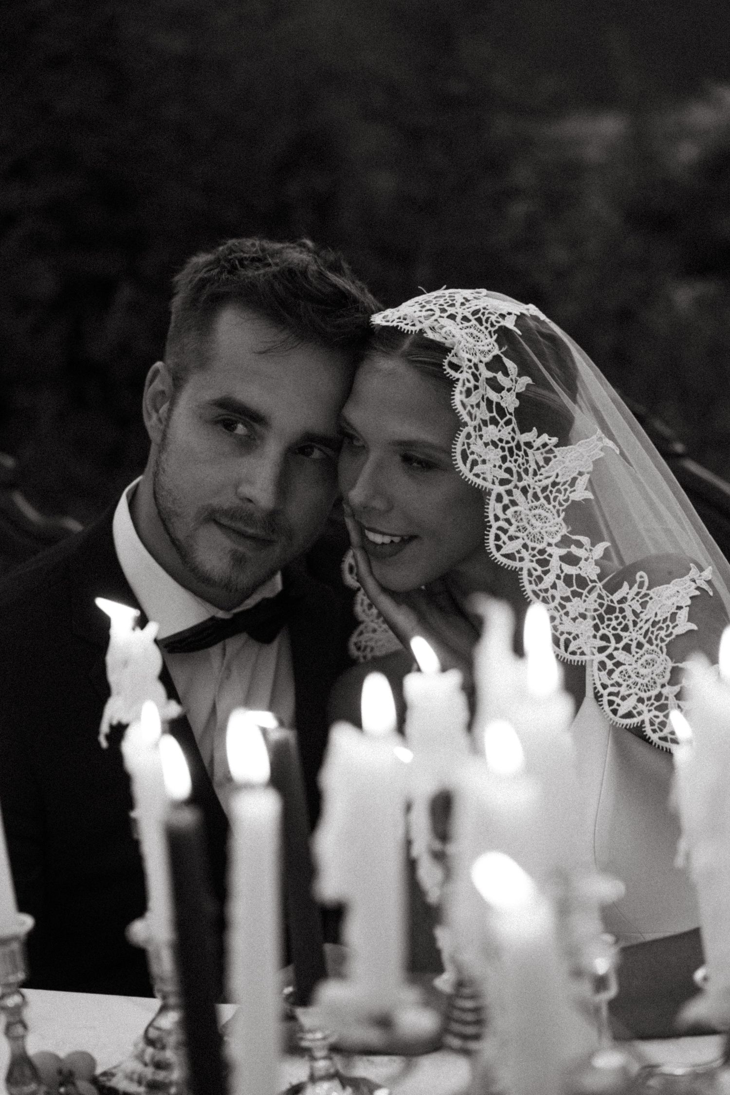 Black and white romantic wedding photograph with candlelit table and delicate lace veil detail.