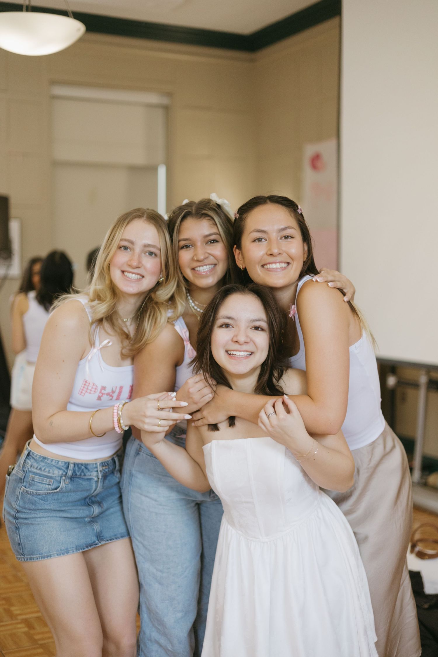 A group of friends embrace and smile together at an indoor gathering wearing casual summer outfits.
