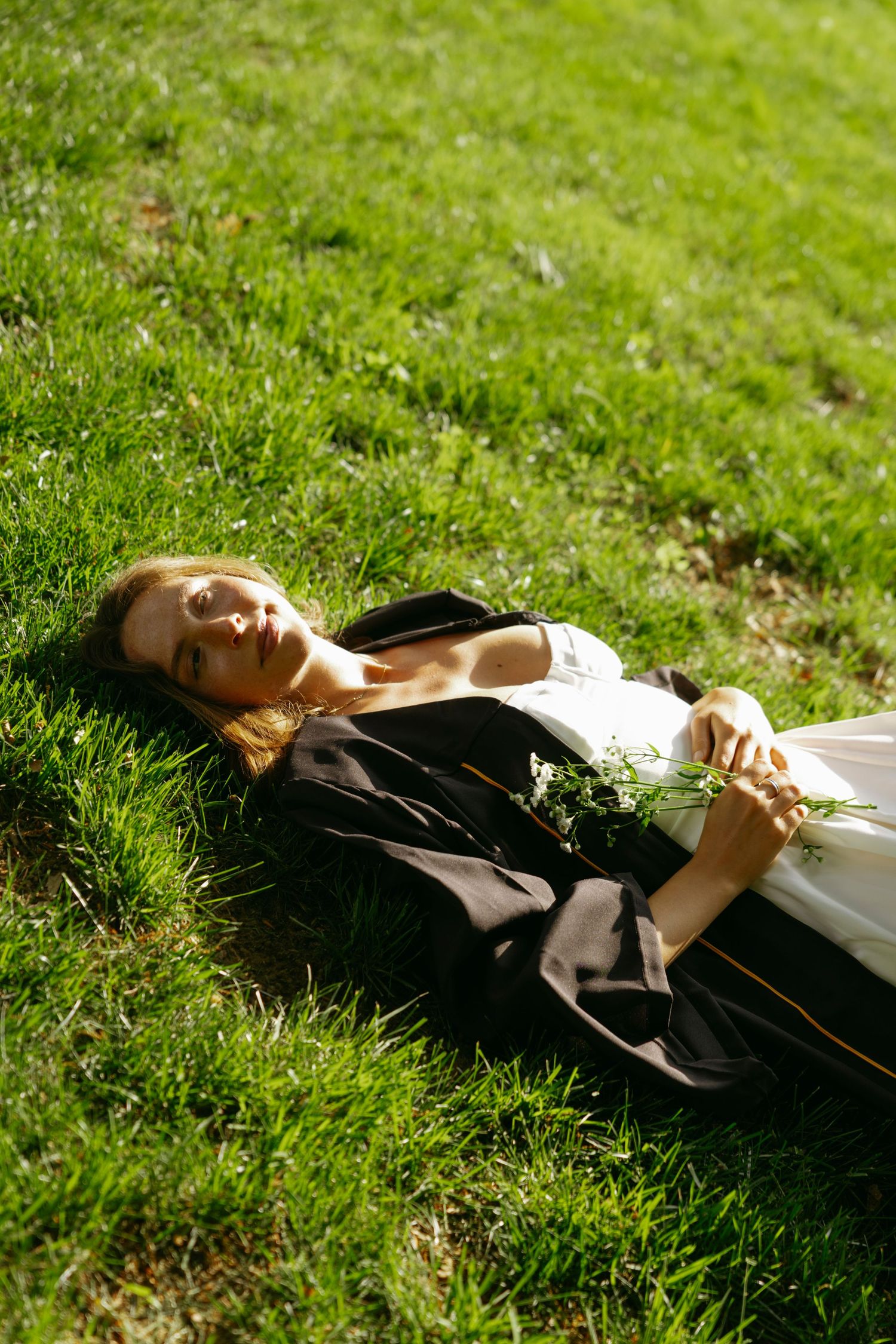 A person in dark clothing lies relaxed on bright green grass in sunlight, creating a peaceful outdoor scene.