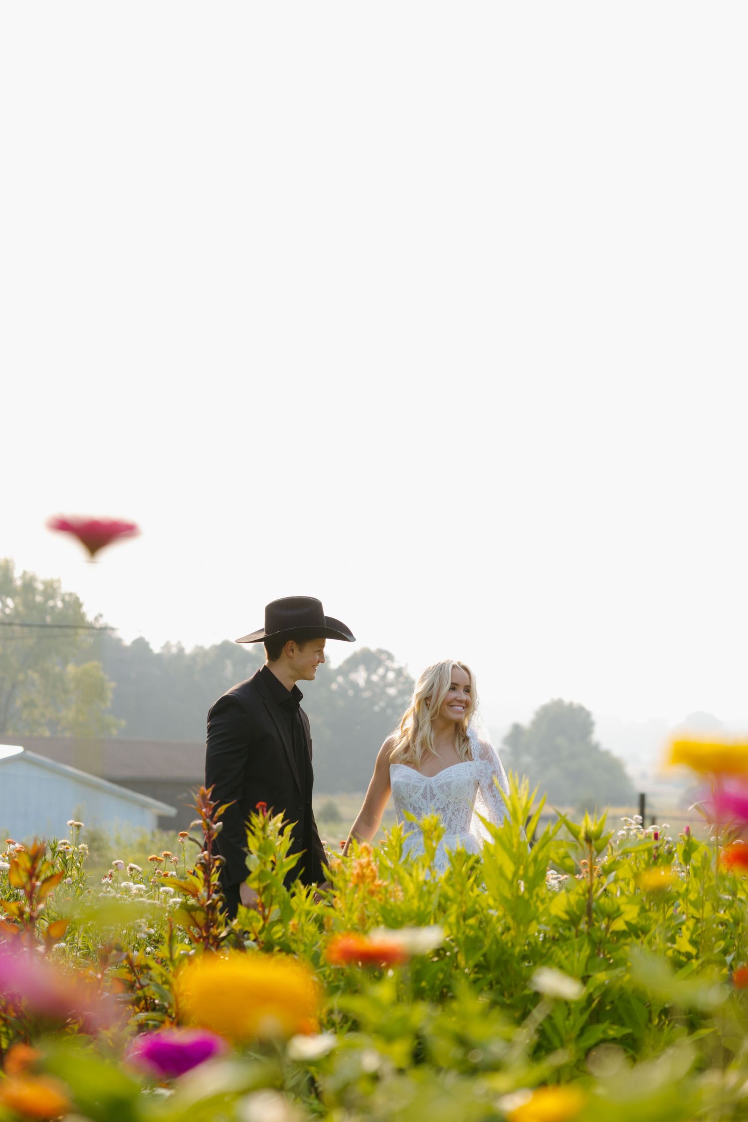 A couple walks through a vibrant wildflower field on a misty morning with colorful blooms in the foreground.