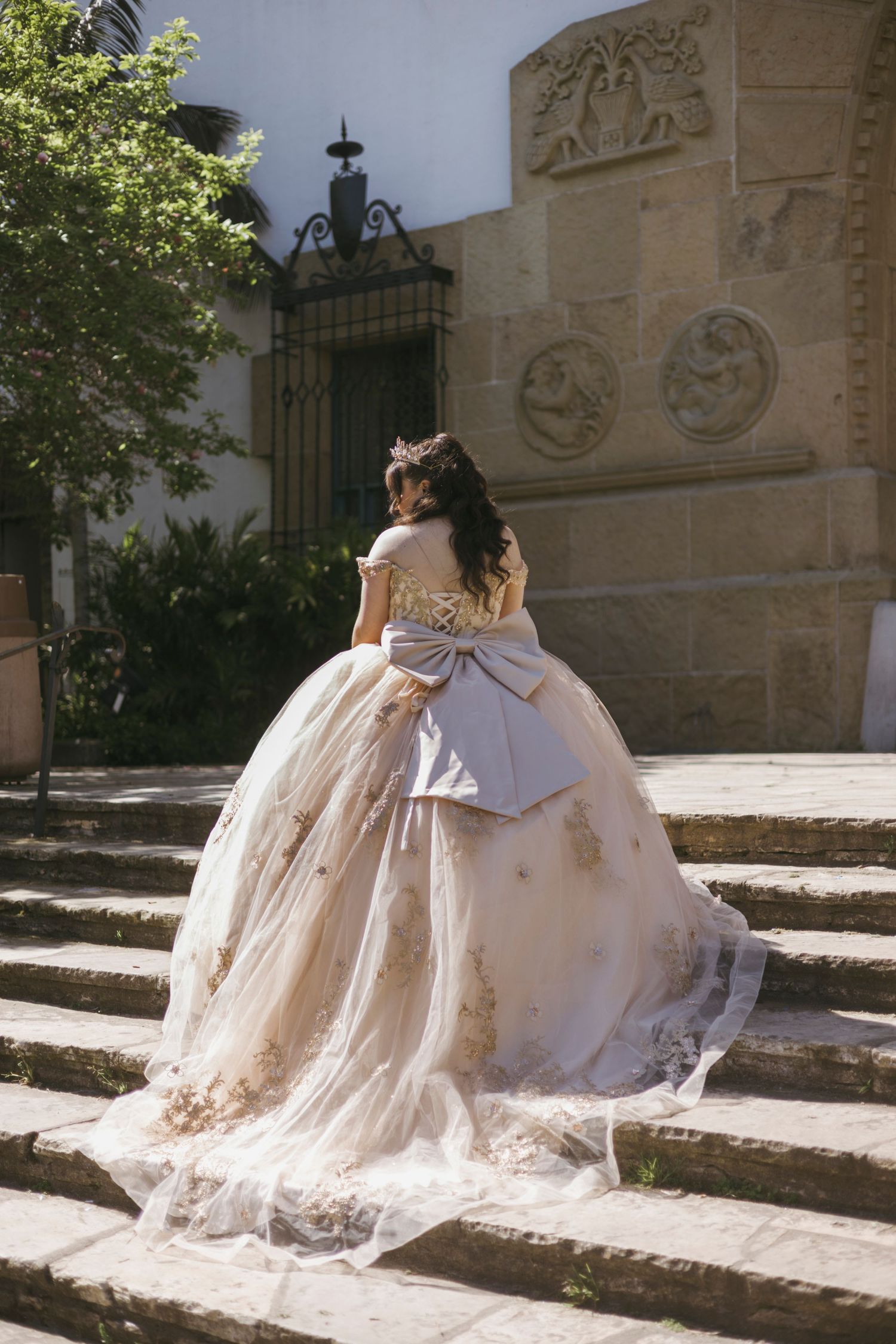 Women in matching elegant bridal gowns sit together on stone steps in an ornate architectural setting.