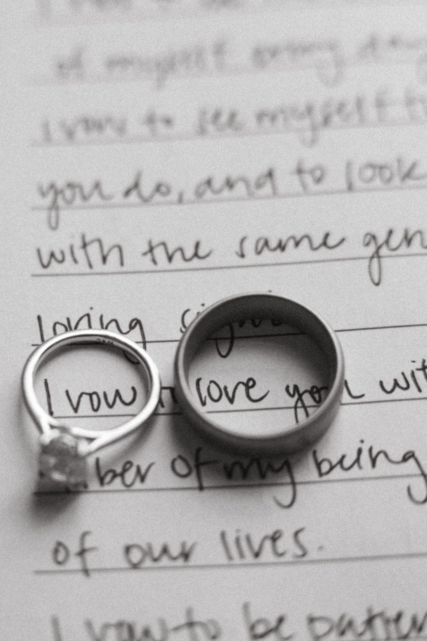 A handwritten word 'love' is shown through wedding rings casting shadows on a white paper surface.
