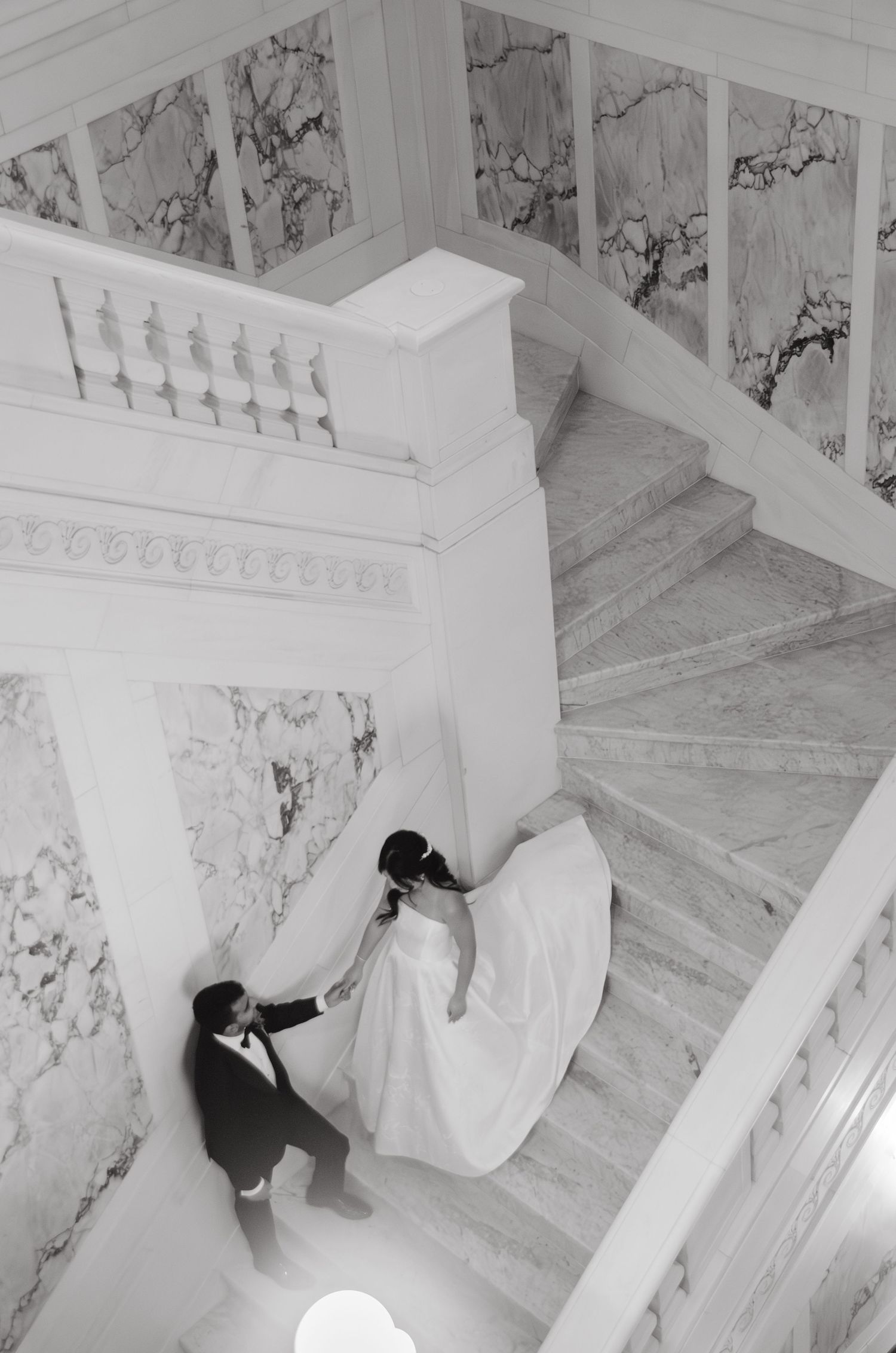 Aerial view of couple walking down marble staircase with flowing white dress.