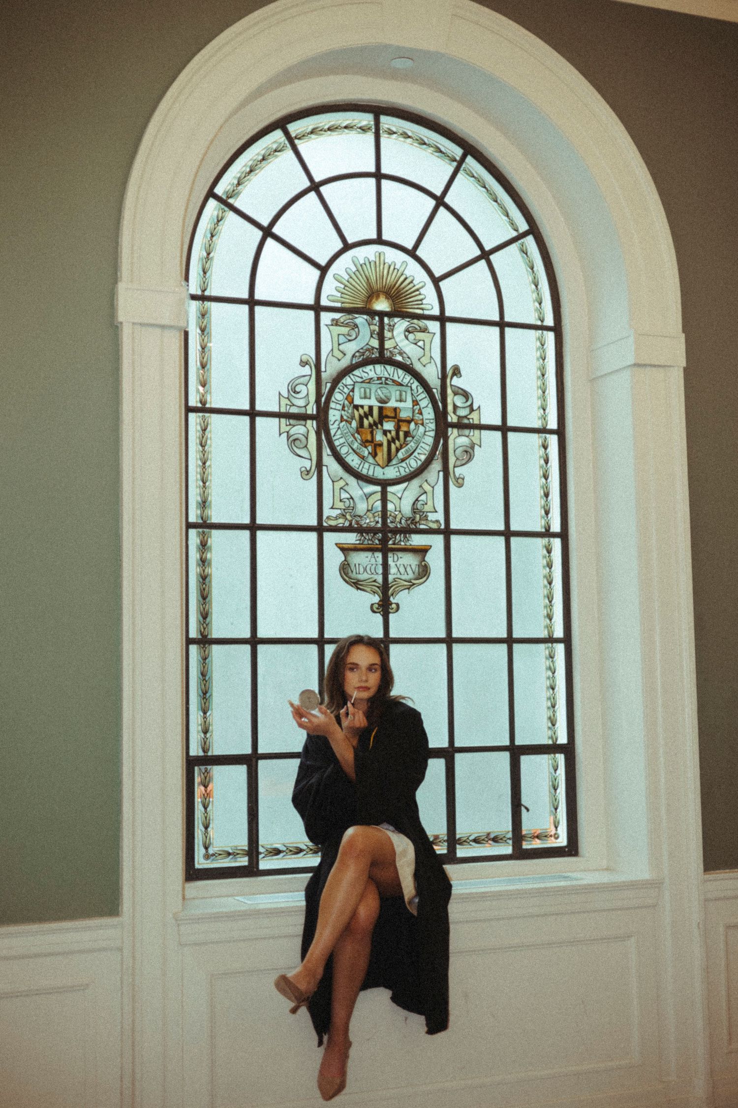 A person in black sits elegantly on an ornate stained glass window ledge in a light-filled architectural space.