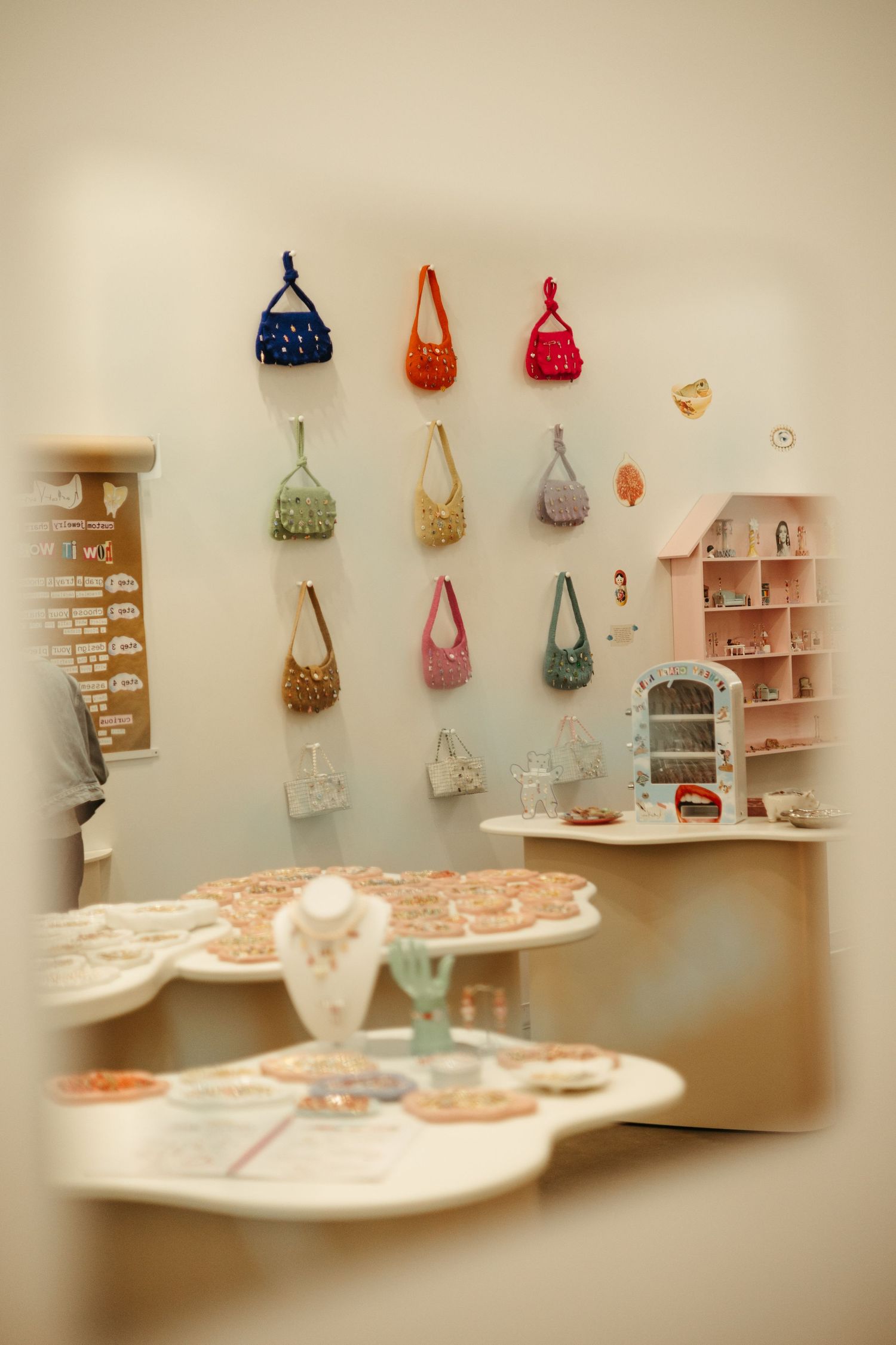 A retail display showing colorful handbags hung on a wall near decorative shelves and showcases with jewelry.