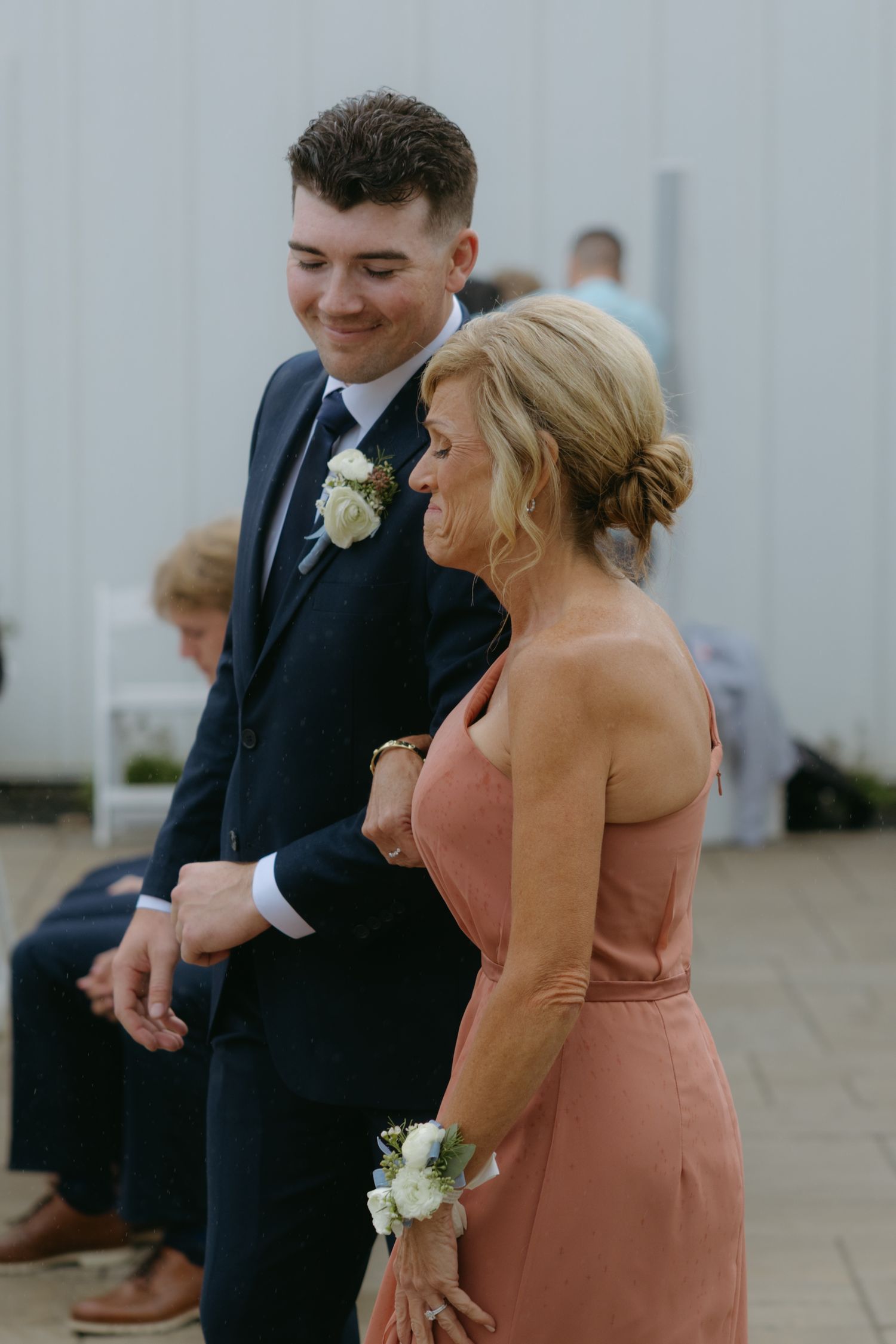 Wedding attendants in formal attire share a joyful moment, with a groomsman in navy suit and bridesmaid in peach dress.