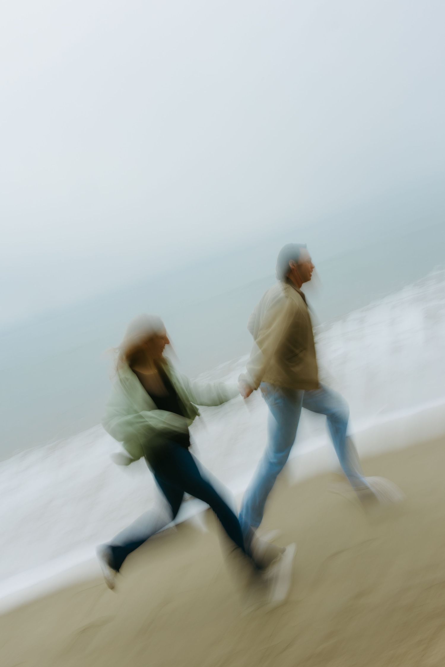Motion blurred figures walking along a misty beach shore with soft dreamy atmospheric effect.