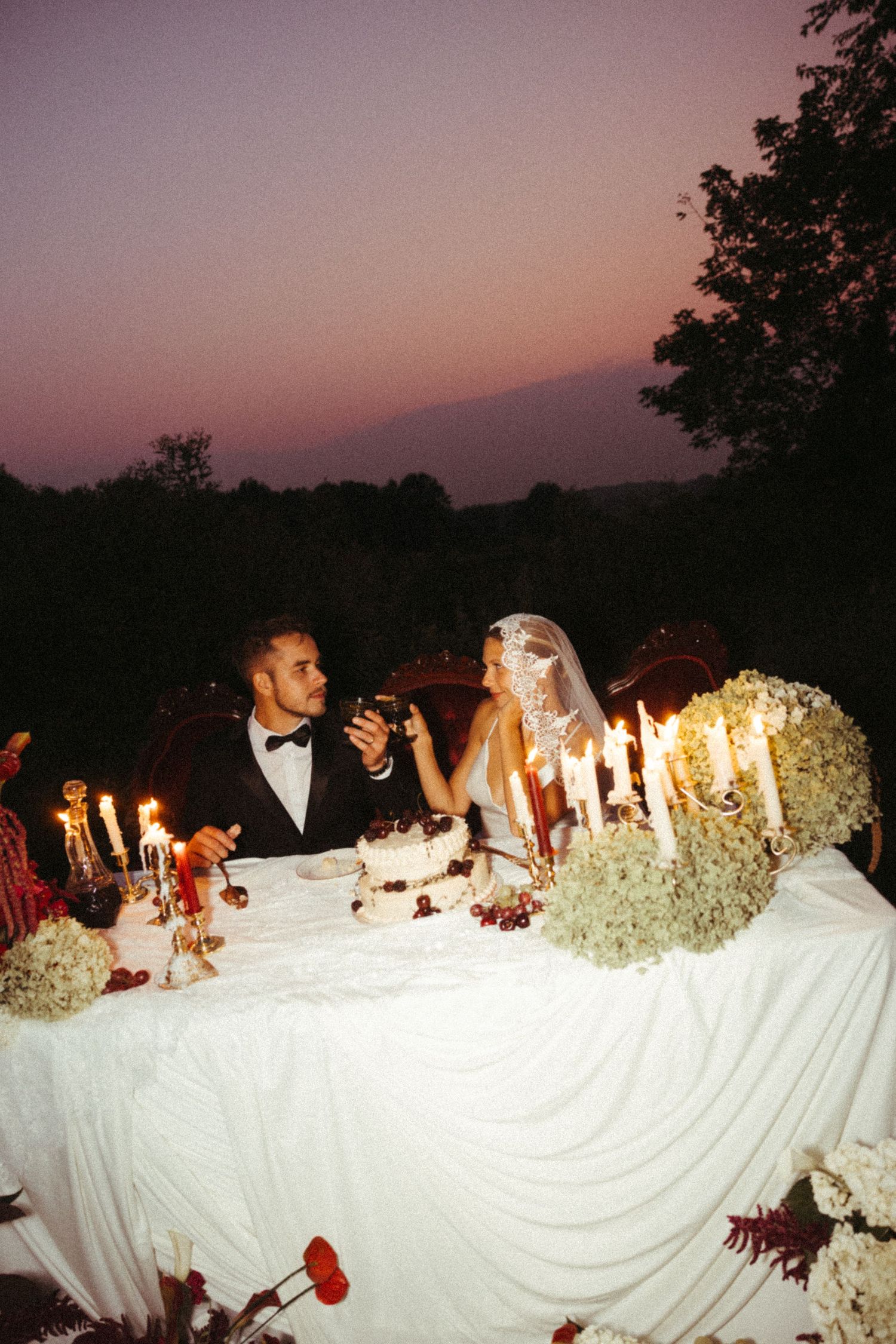 Wedding tablescape with white linens and glowing candles creates a romantic ambiance at dusk.