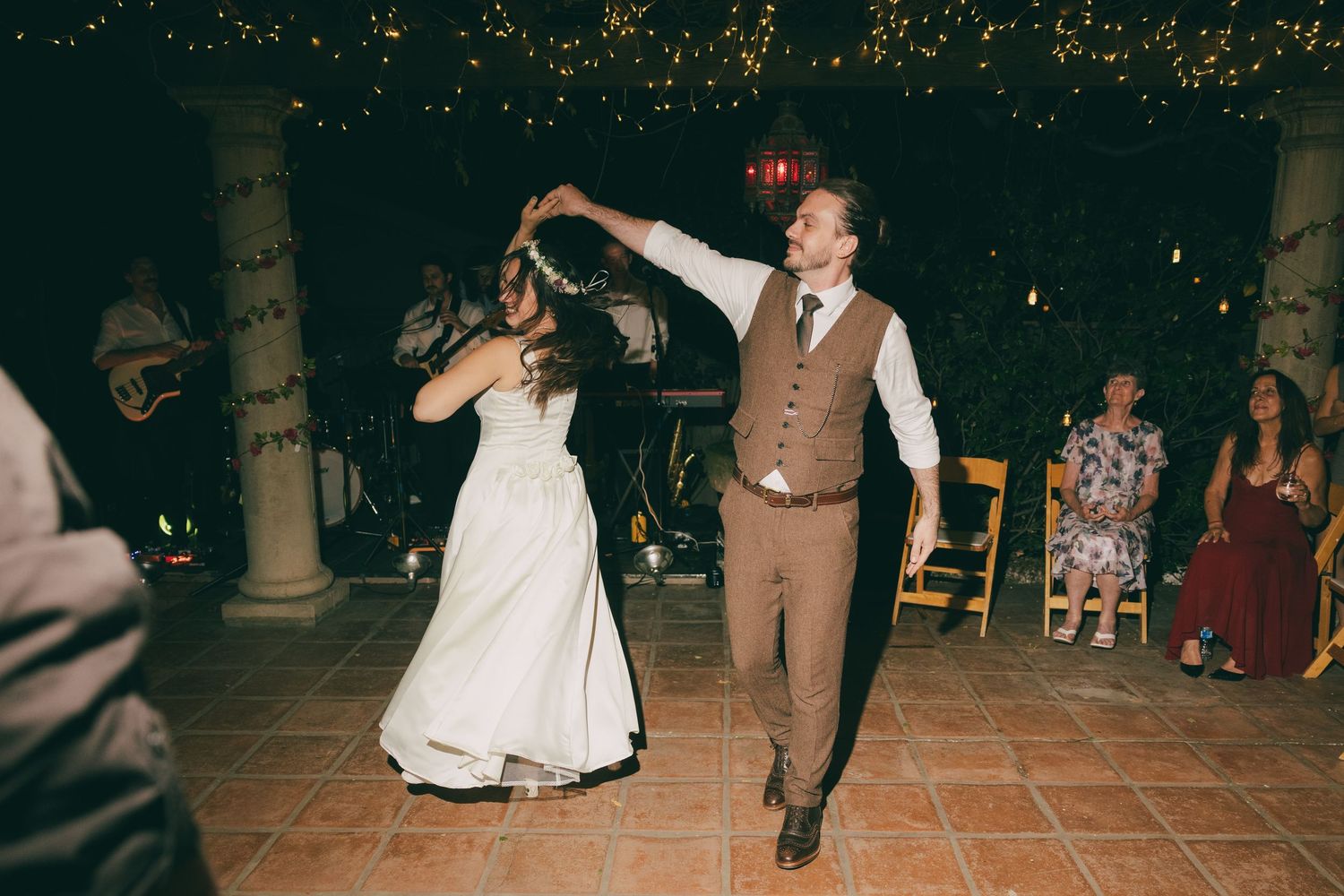 Bride and groom share a romantic first dance at an outdoor evening wedding reception under twinkling string lights.