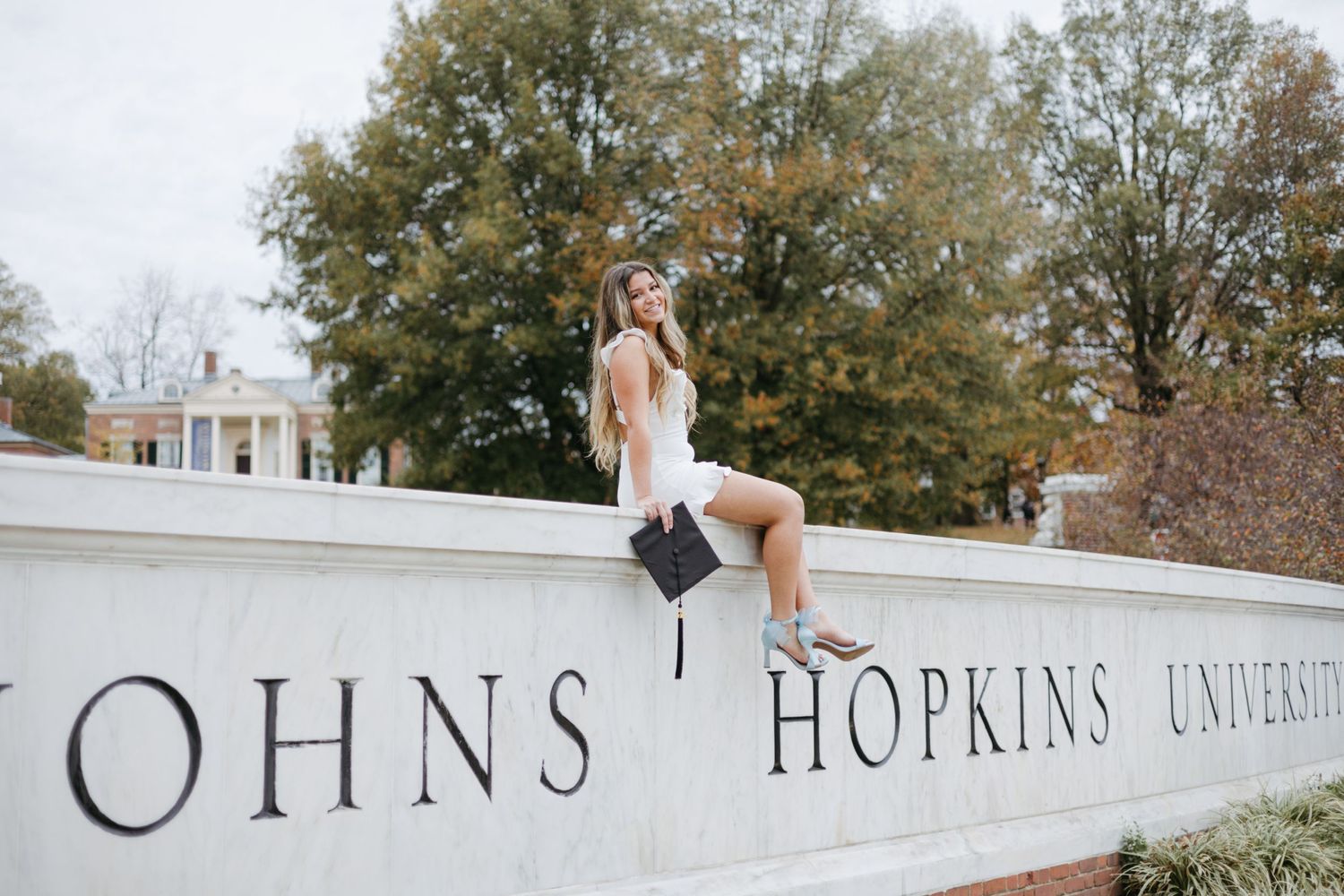 Graduate sits on Johns Hopkins University sign during graduation photoshoot.
