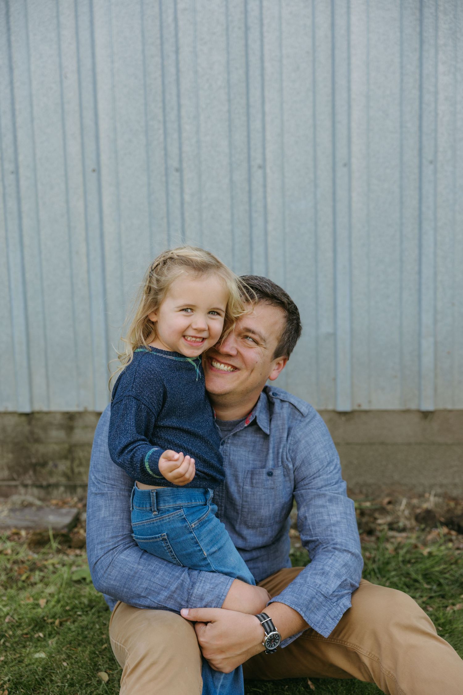 A parent and child in matching denim share a joyful moment together against a corrugated wall background.