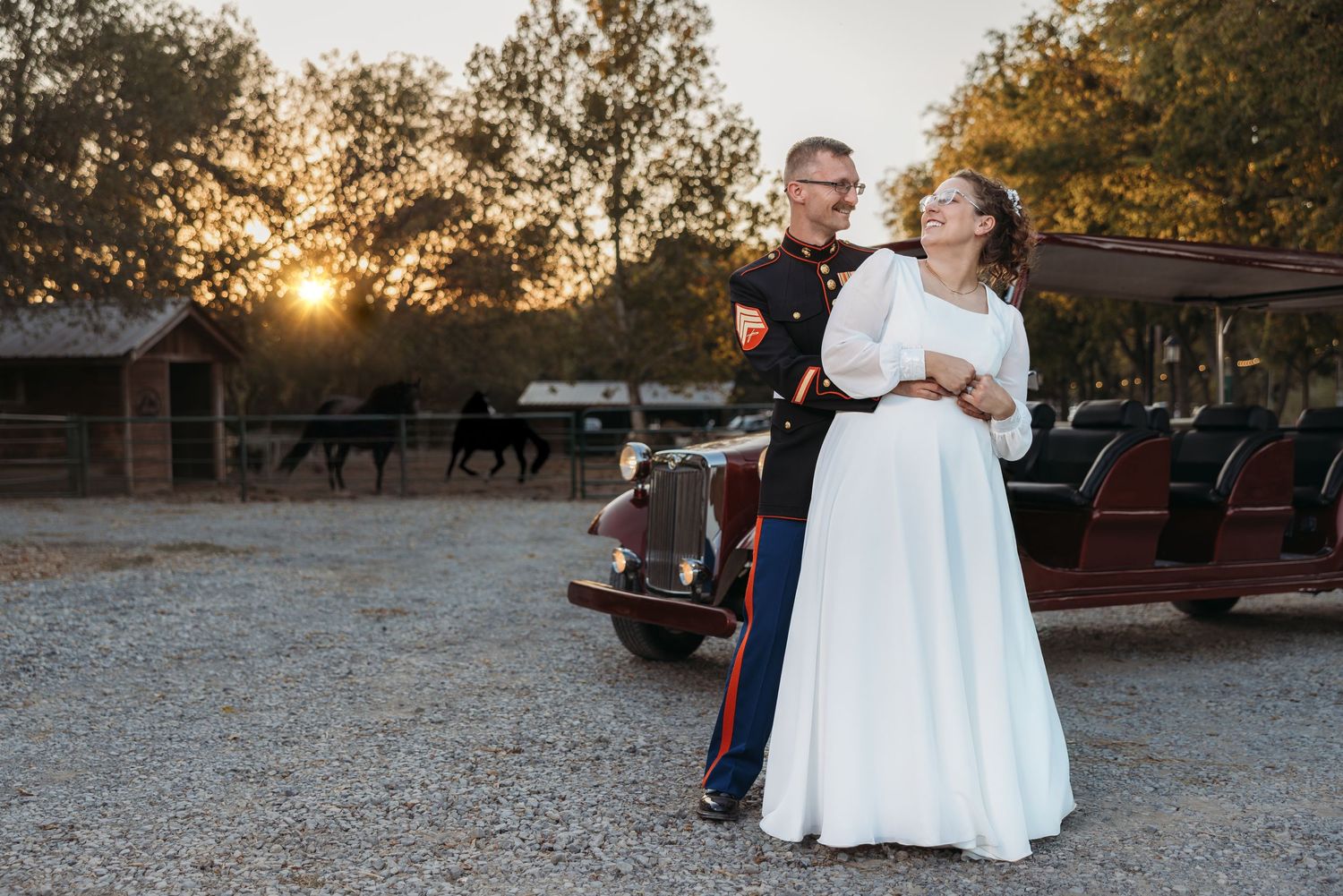 Marine groom and bride posing together at sunset near a vintage car at an outdoor ranch venue.