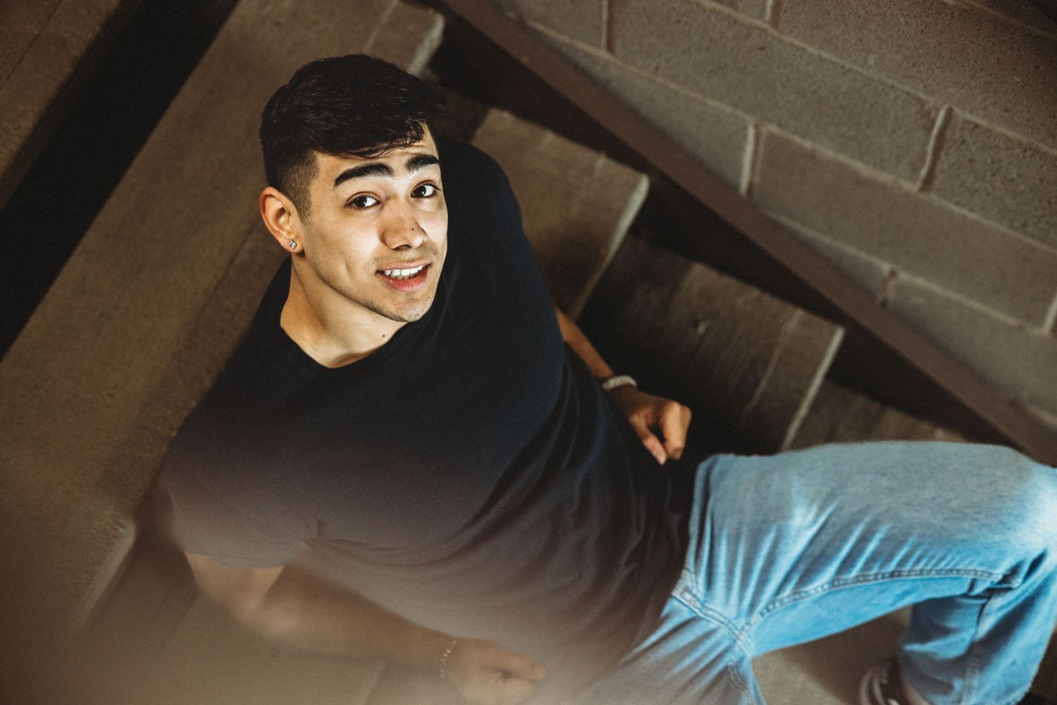 Young man in black shirt sitting on stairs looking up at camera.