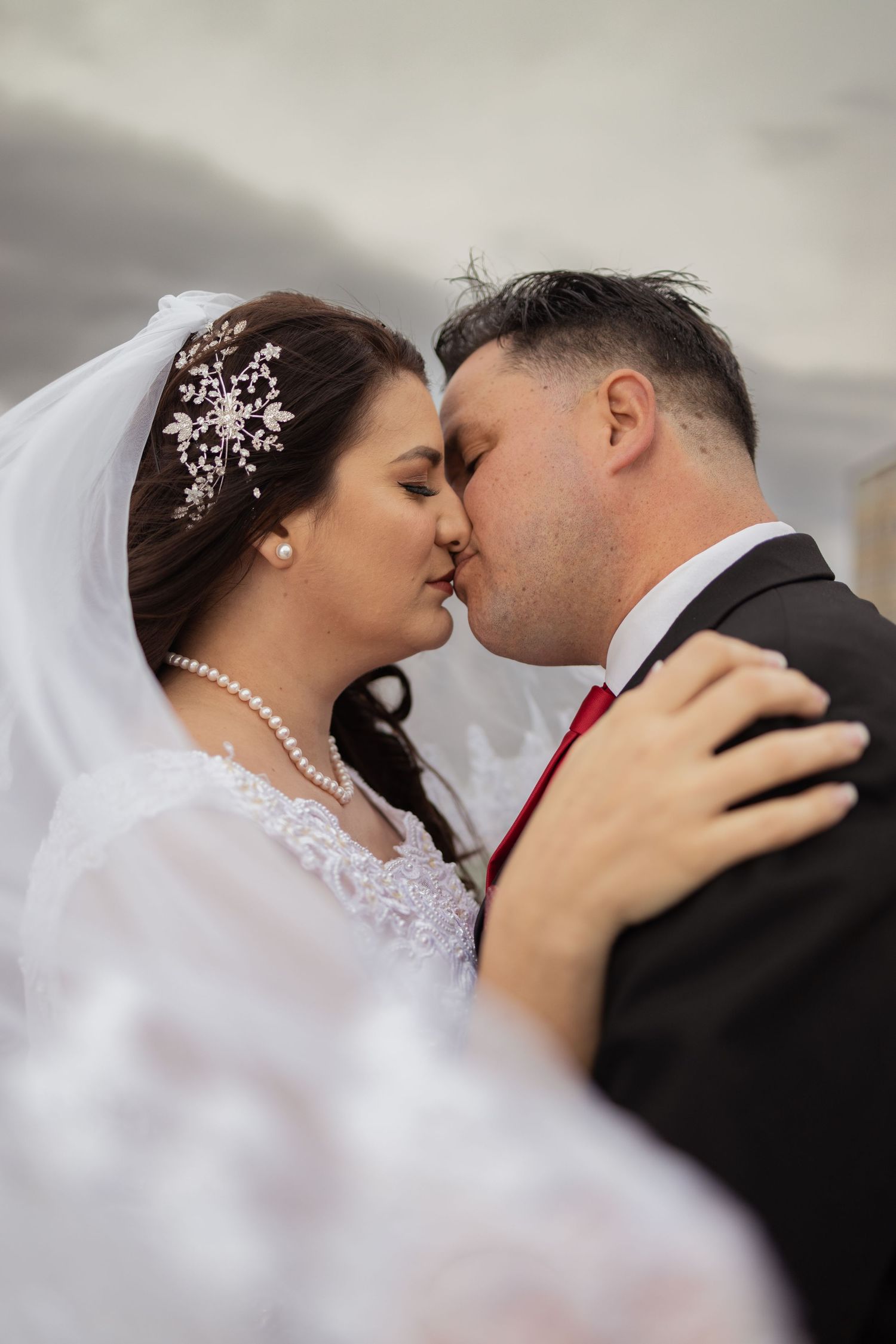 Bride and groom sharing first kiss outdoors with dramatic cloudy sky.