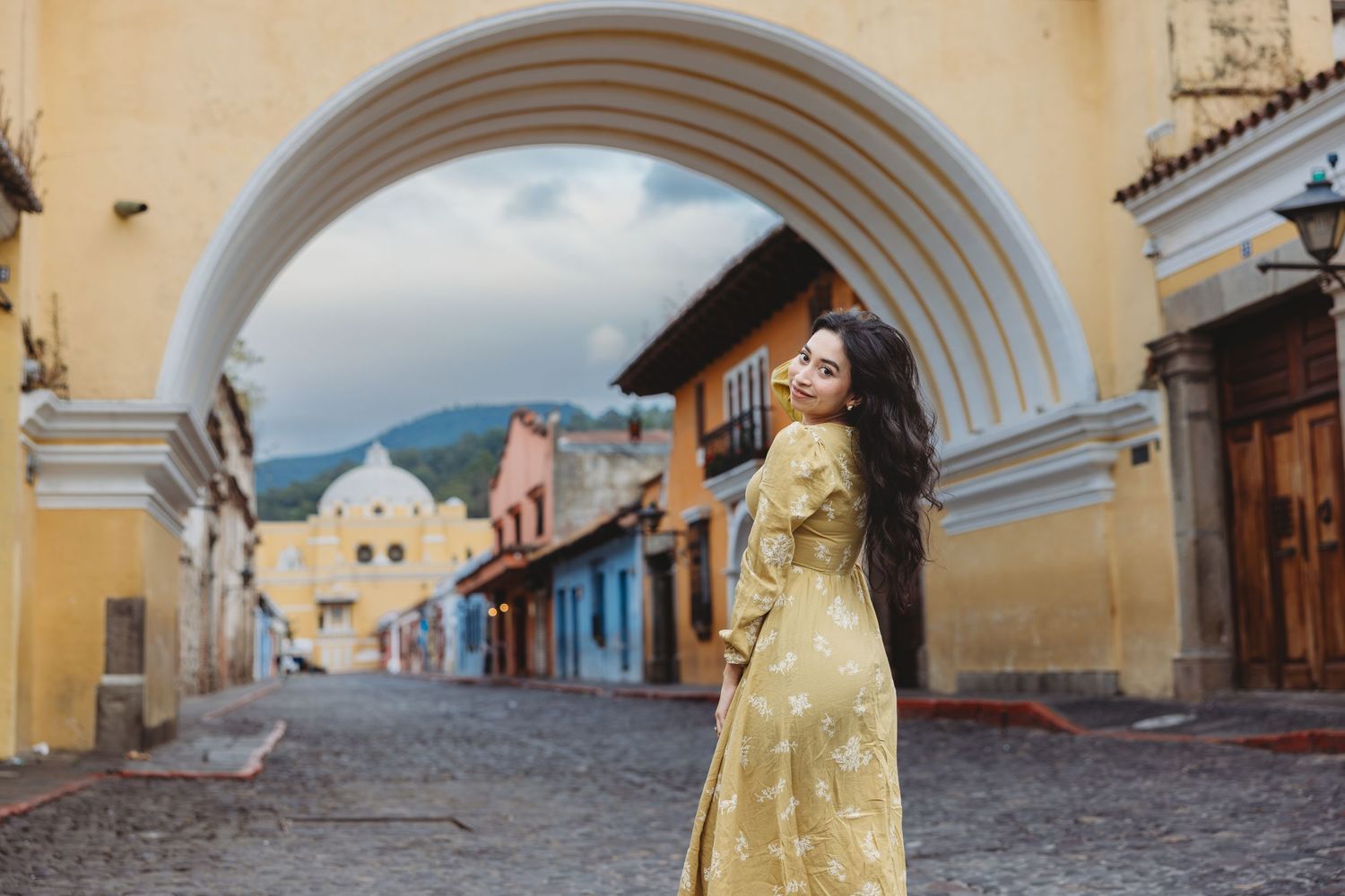 Woman in gold dress posing under iconic Santa Catalina arch in Antigua, Guatemala.