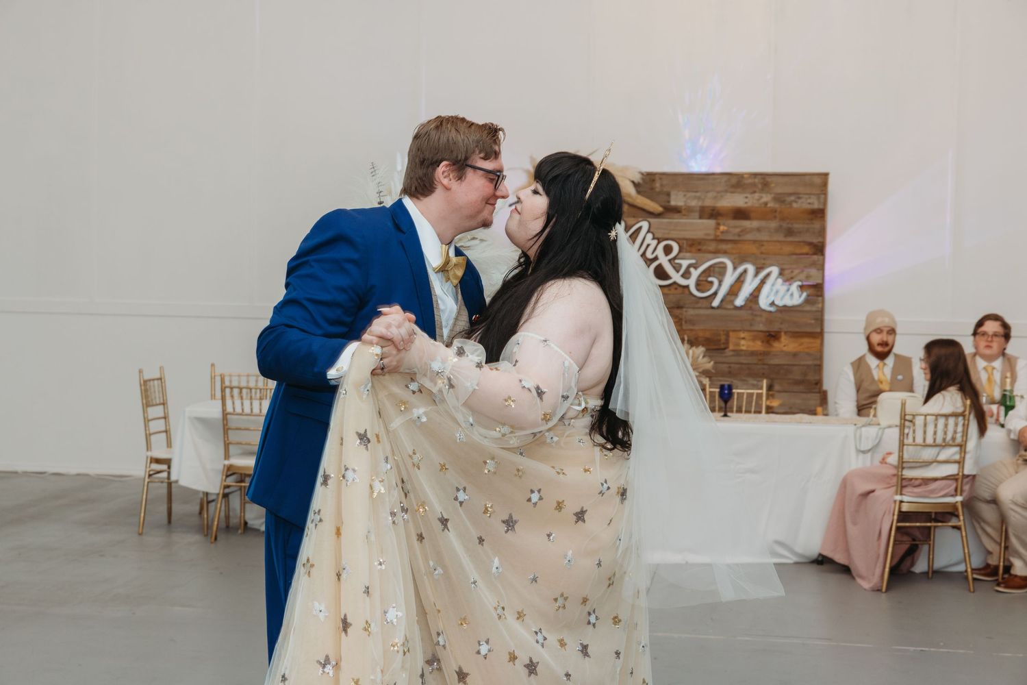 Bride and groom sharing their first dance kiss in front of a Mr. and Mrs. wooden backdrop.