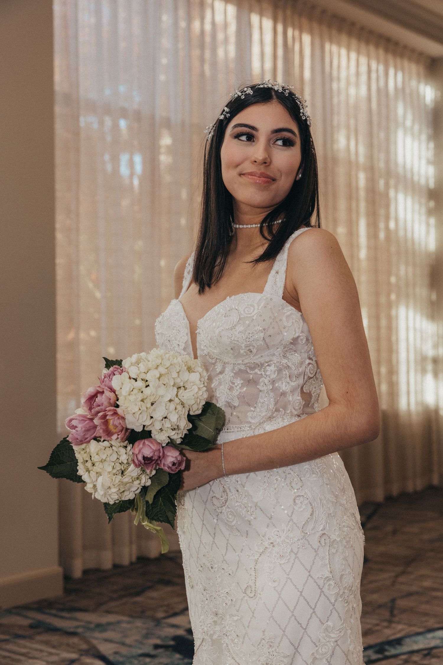 Bride in a beaded white wedding gown holding a bouquet of white and pink flowers.