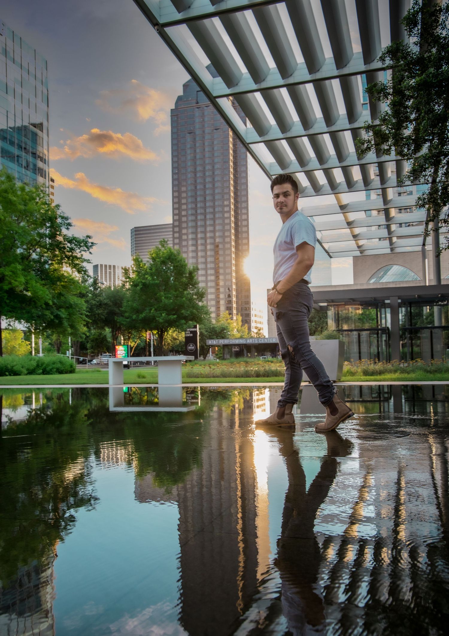 Man walking near reflective pool at sunset with city skyline in background.